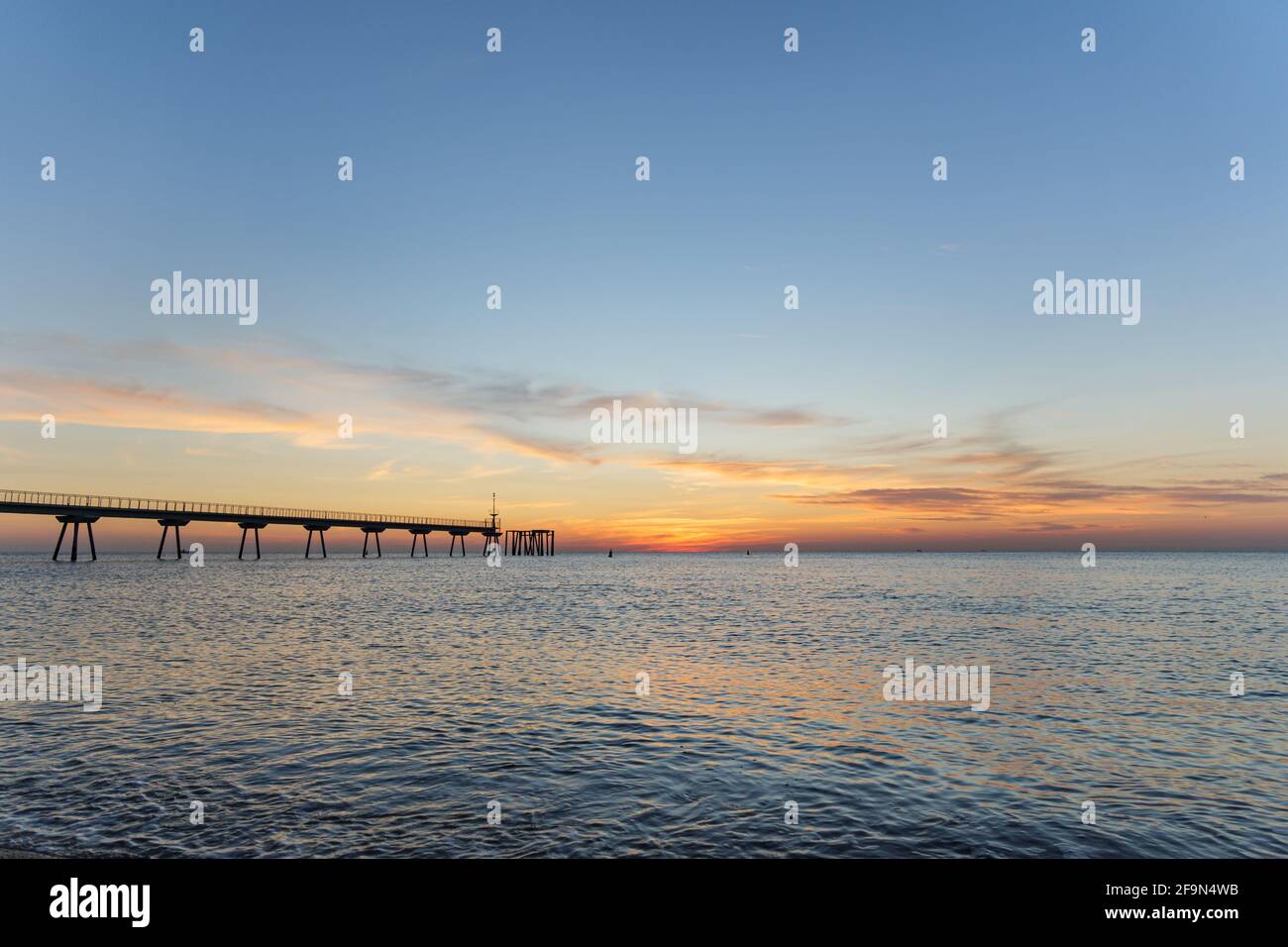 Am frühen Morgen ein paar Minuten vor Sonnenaufgang. Sonnenaufgang auf dem Meer mit Ponton. Der blaue Himmel ist in Orange gehalten. Stockfoto