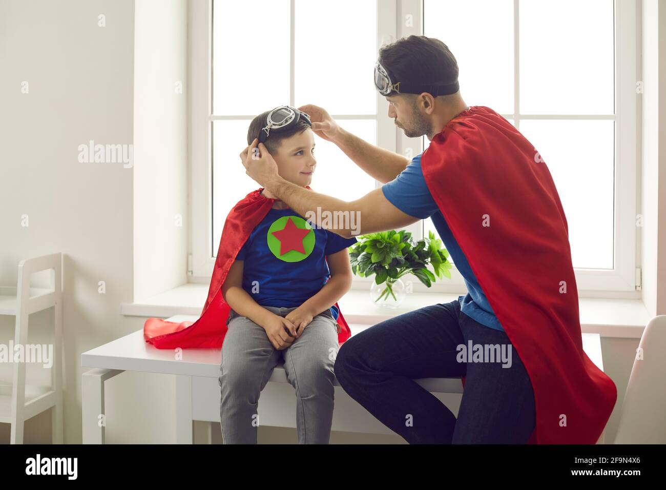 Papa hilft Sohn setzen auf Fliegerbrille beim Spielen Spaß Superhelden-Spiele zu Hause Stockfoto