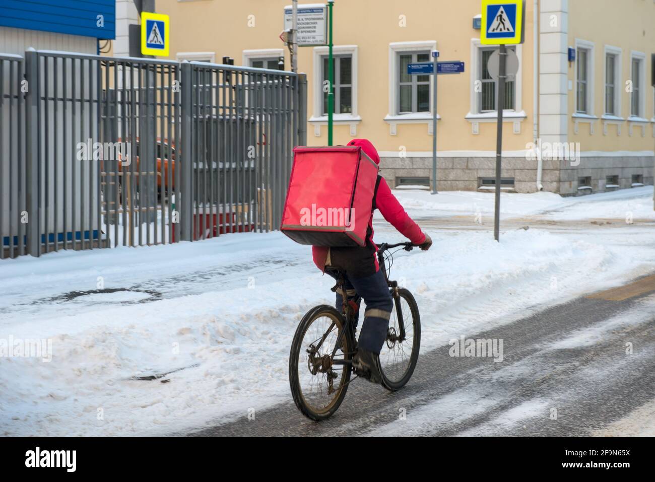 Moskau, Russland - 17. Januar 2021: Lebensmittellieferer auf dem Fahrrad, der im Winter an einem frostigen Wintermorgen nach einer schweren Schneepfanne auf der schmutzigen Stadtstraße arbeitete Stockfoto