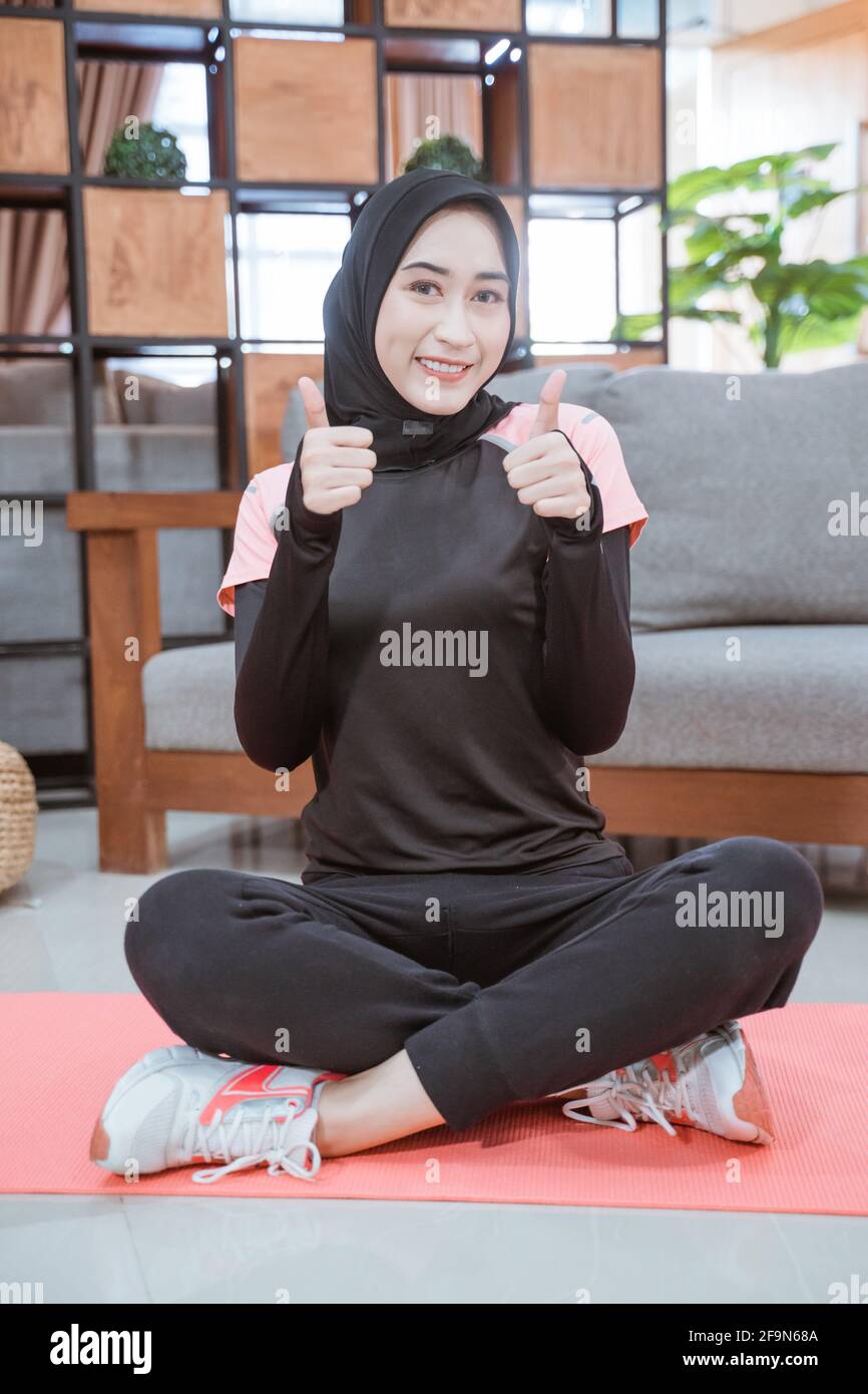 Nahaufnahme einer muslimischen Frau in einem Hijab-Workout-Outfit Sitzt mit  gekreuzten Beinen und Daumen nach oben auf dem Boden Stockfotografie - Alamy