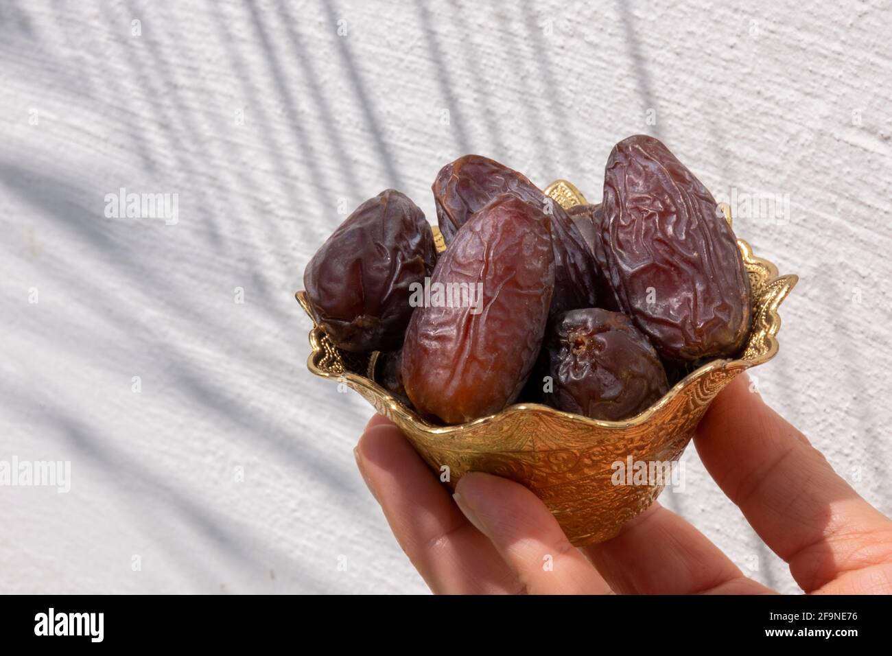 Religiöses muslimisches Fastenfest und heiliger Monat des Ramadan Konzept: Eine Hand hält eine verzierte Metallschale mit braunen getrockneten Dattdaten-Früchten. Palmenblatt Stockfoto