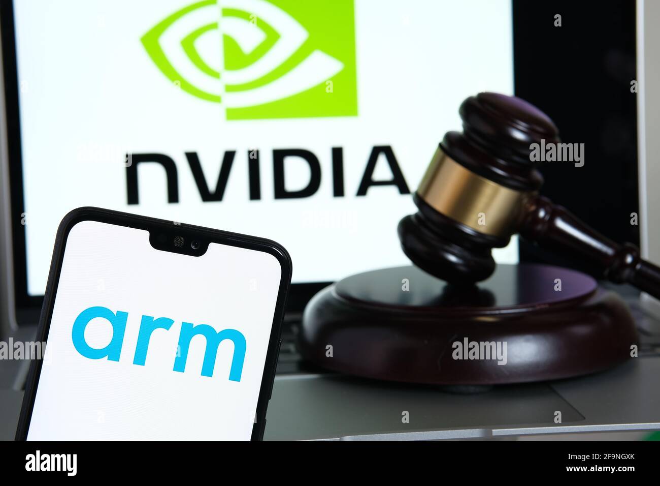 ARM-Firmenlogo auf dem Smartphone, gavel und NVIDIA-Logo auf dem unscharfen Apple M1 ARM-basierten Laptop-Bildschirm. Konzept für Firmenakquisition und eine Stockfoto