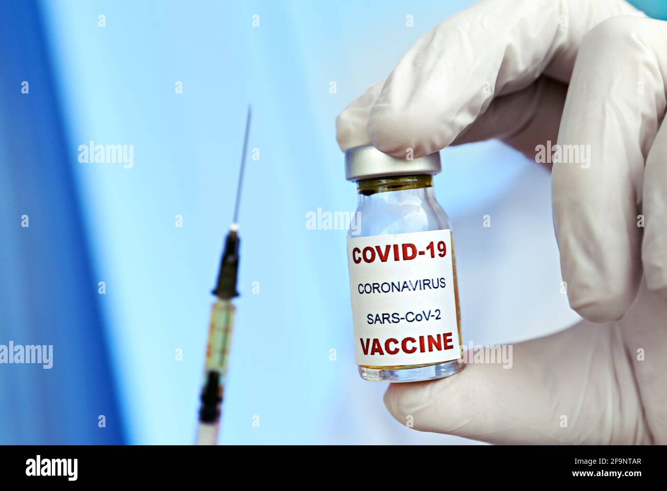 Makroaufnahme der Hände eines Arztes in blauen Latexhandschuhen mit dem neuen Covid-19-Impfstofffläschchen und der mit Medikamenten gefüllten Oberfläche. Nahaufnahme, Kopierbereich, Backgr Stockfoto