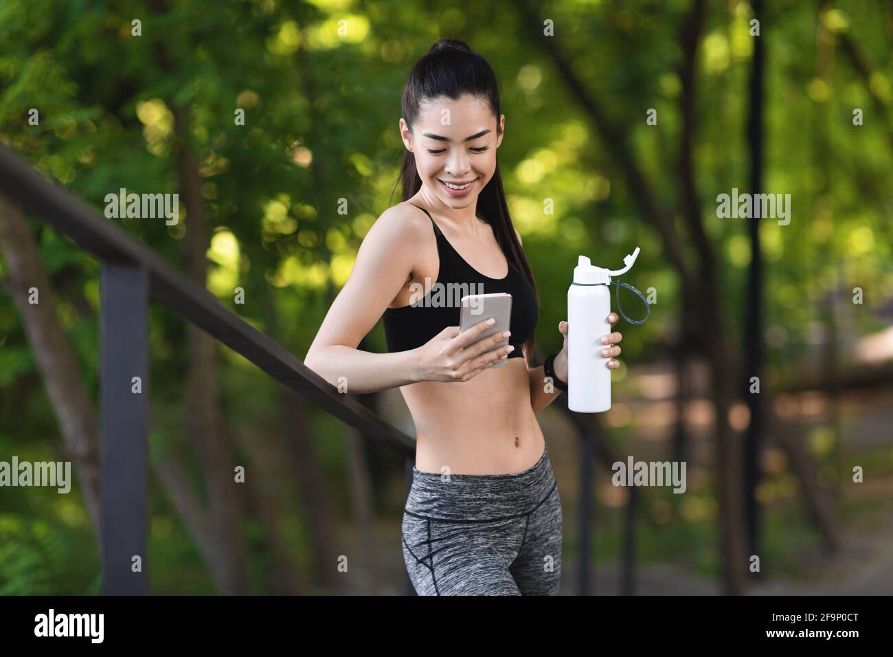 Junge Asiatische Mädchen Mit Smartphone Und Trinkwasser, Ruhe Nach Outdoor-Workout Stockfoto