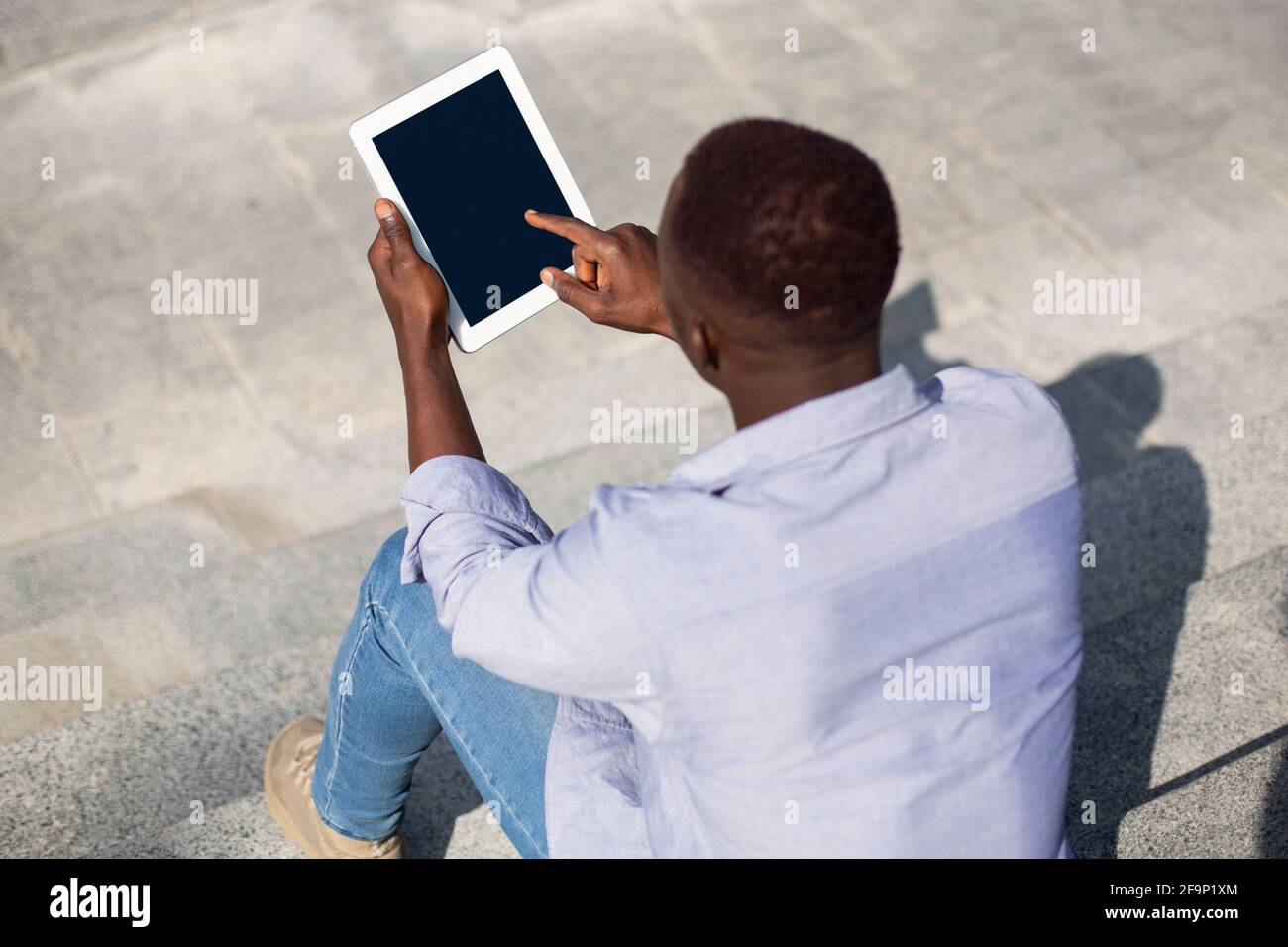 Junger schwarzer Kerl mit Tablet-Computer mit leerem Bildschirm auf Steintreppen im Freien, Mockup für Website-Design Stockfoto