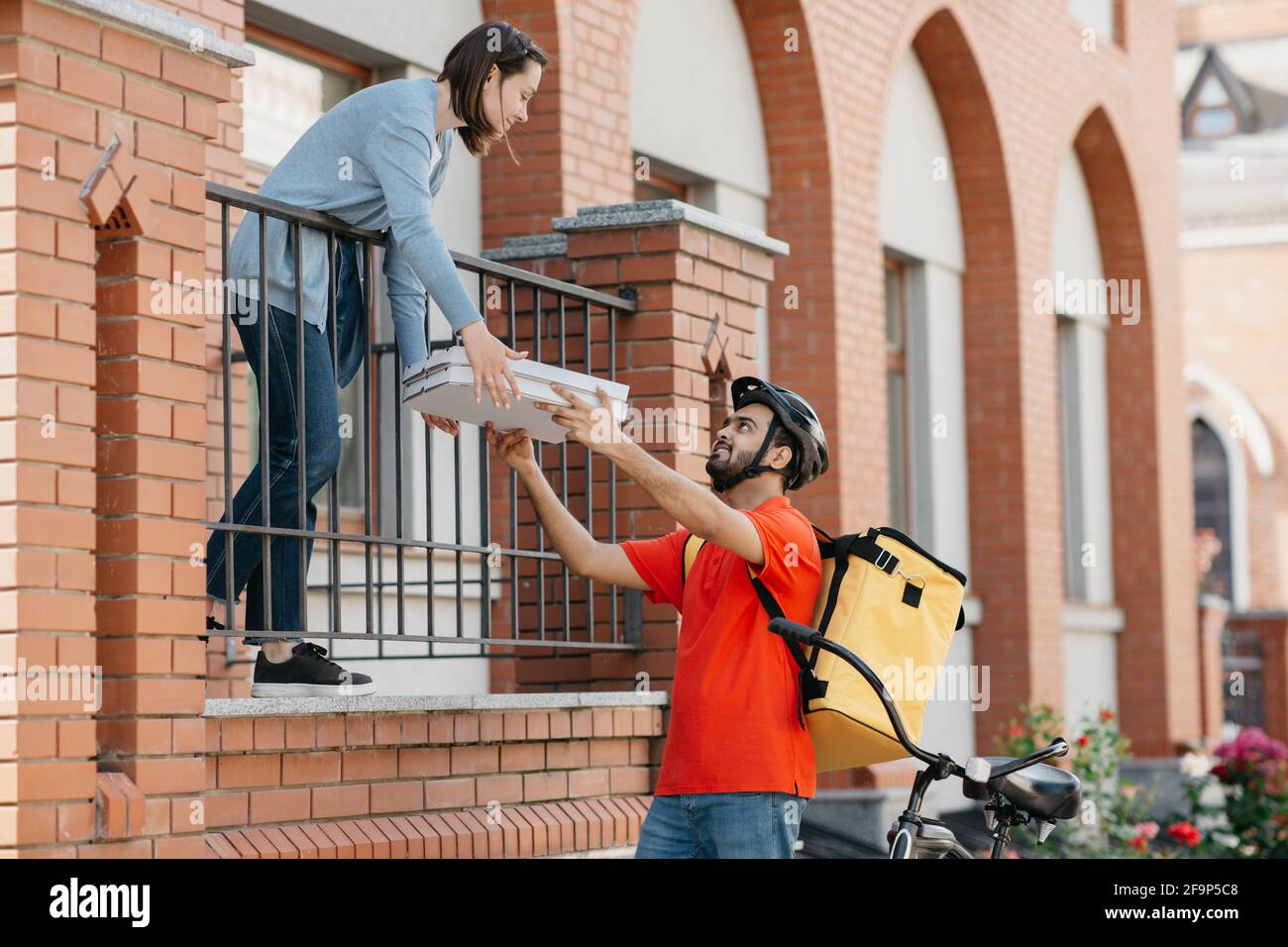 Indischer Tausendjähriger freundlicher Kerl gibt weiblichen Kunden Boxen mit Pizza Stockfoto