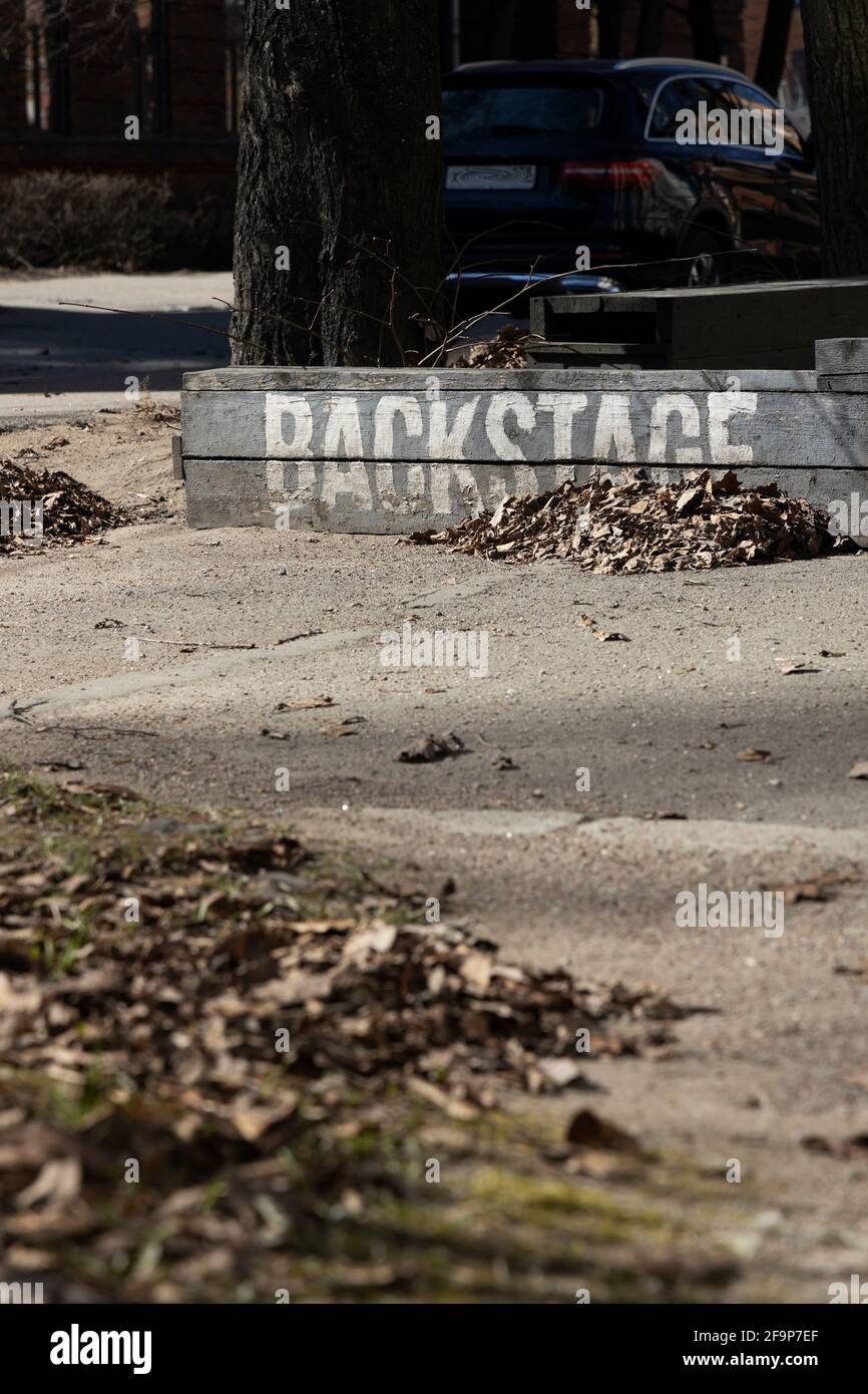 Dunkle Straßenbank mit der weißen Aufschrift 'Backstage' mit einem Haufen trocken gefallener Blätter vertikal ausgerichtet Stockfoto