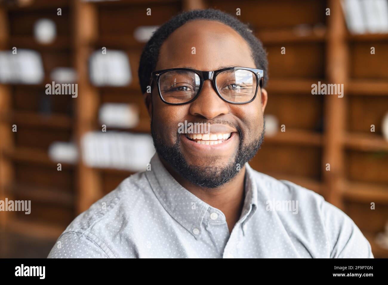 Nahaufnahme eines glücklichen afroamerikanischen jungen Mannes mit freundlichem, weit toothy Lächeln, ein bärtiger Mann mit gemischter Rasse in stilvoller Augengasse und Hemd blickt in die Kamera, Mitarbeiterprofil Stockfoto