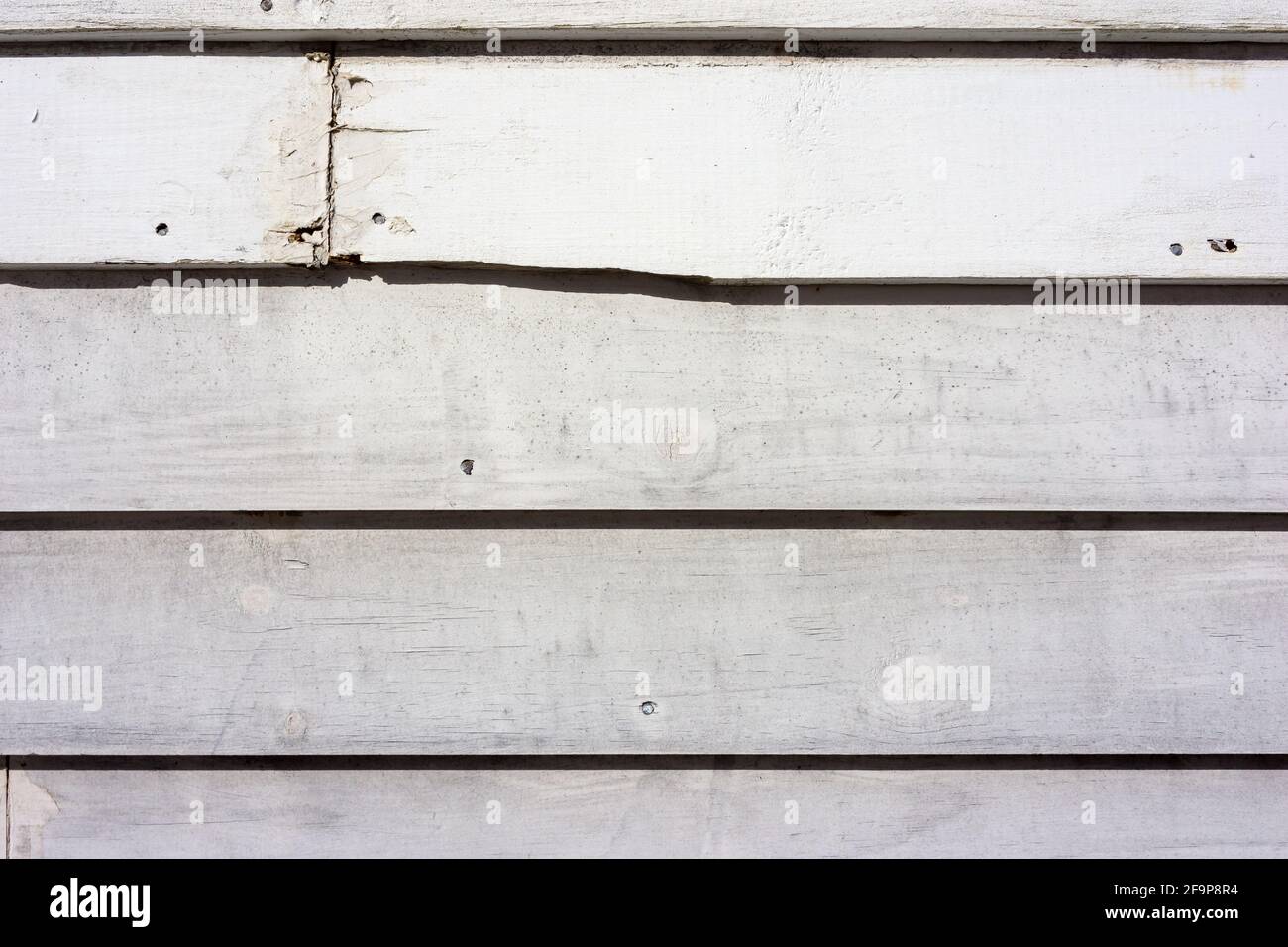Alte Klapptafel, die weiß gestrichen war, mit Rissen und einem zerbrochenen Brett im Morgenlicht. Stockfoto
