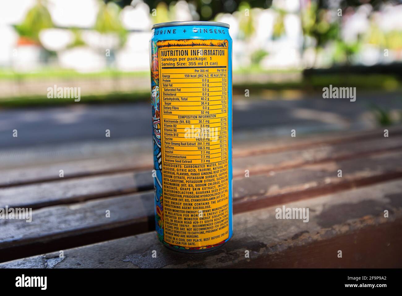 Monster Energy kann trinken, indem sie Nährwertangaben auf der Bank im Freien anzeigt. Stockfoto