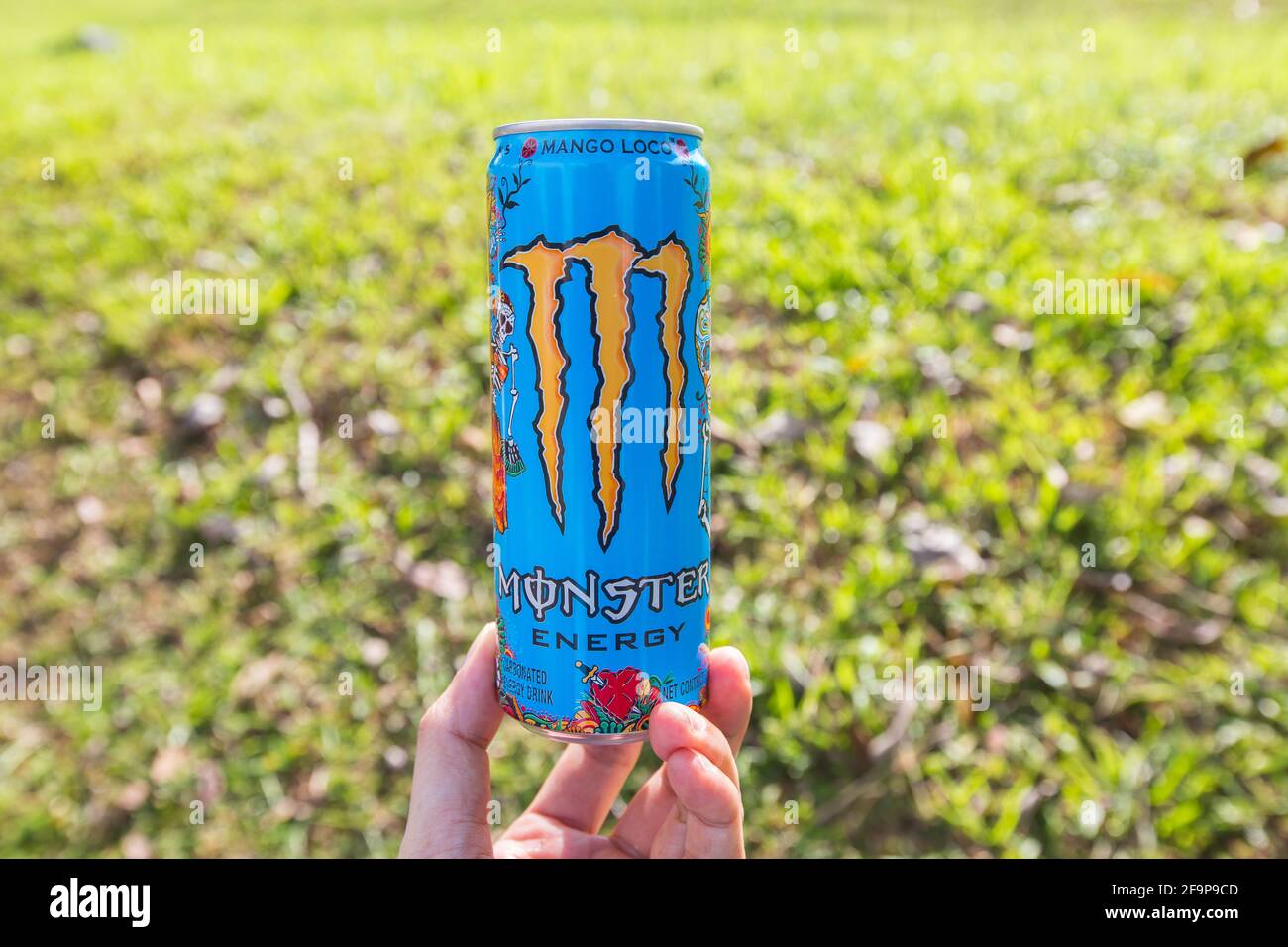 Eine Hand, die die Basis des Monster Energy Drinks vor einem grünen Feld hält. Stockfoto