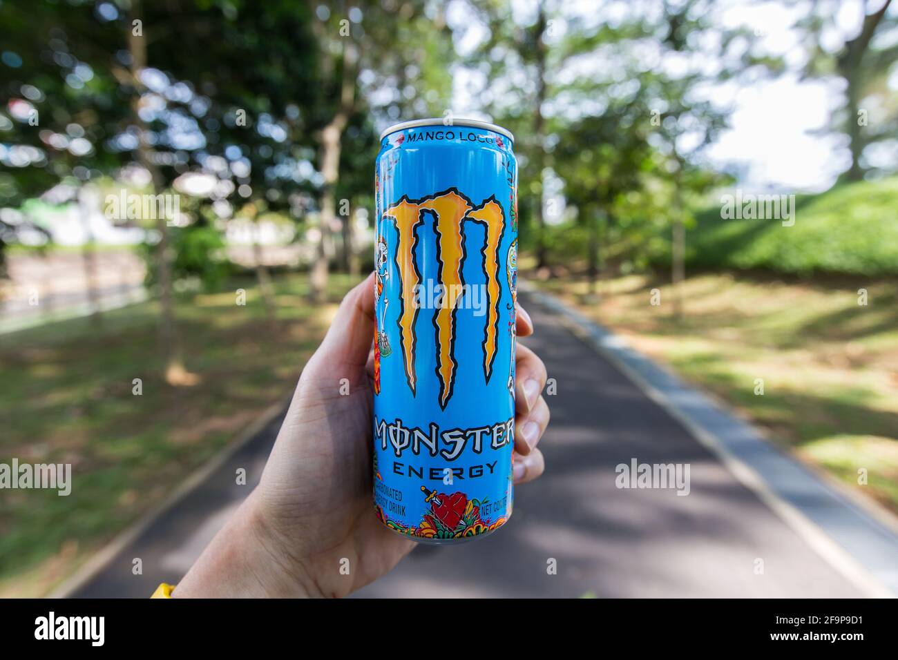 Linke Hand hält einen Mango Loco Monster Energy Drink in der Mitte des Pflasters. Stockfoto