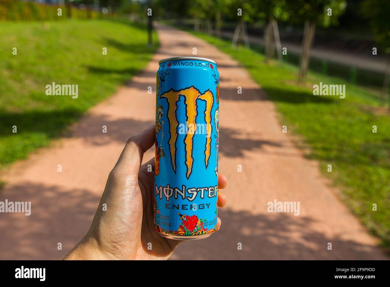 Die linke Hand hält Monster Energy Drink im Freien. Trinke ein Monster, während du auf dem Trail läufst. Energie für schnelleren und längeren Betrieb bereitstellen. Stockfoto