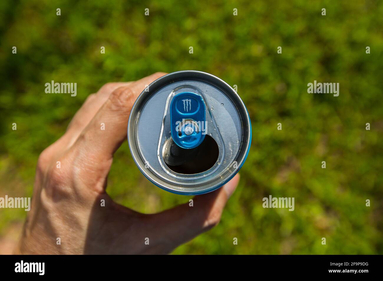 Eine Draufsicht auf eine offene Monster Energy Getränkedose. Bei hellem Licht, Design-Feature auf Zuglasche, grüner Hintergrund im Freien. Stockfoto
