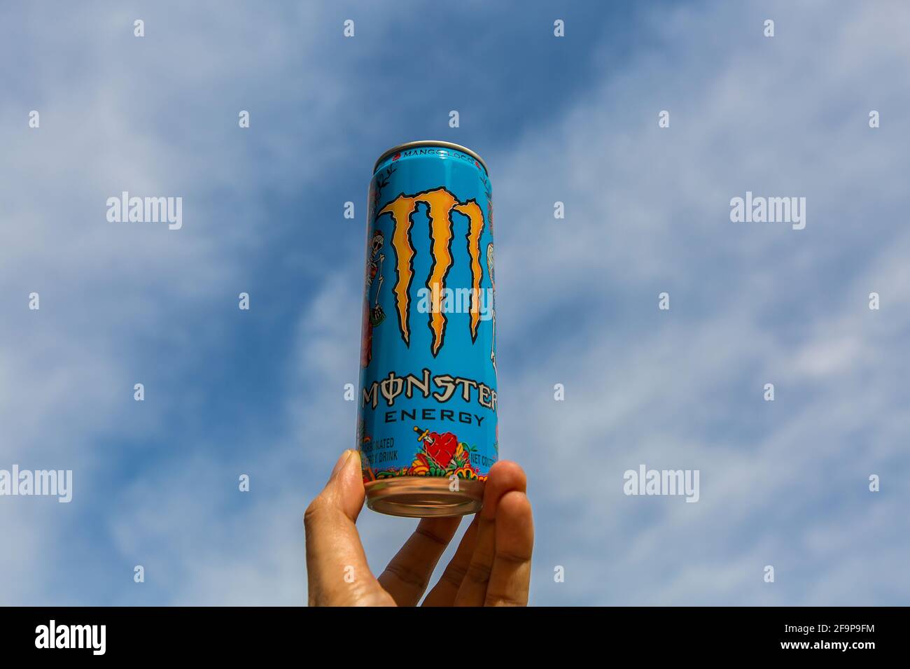 Fingerspitzen, die Monster Energy Drink Dose gegen den wolkenblauen Himmel halten. Mango-Loco-Geschmack. Stockfoto