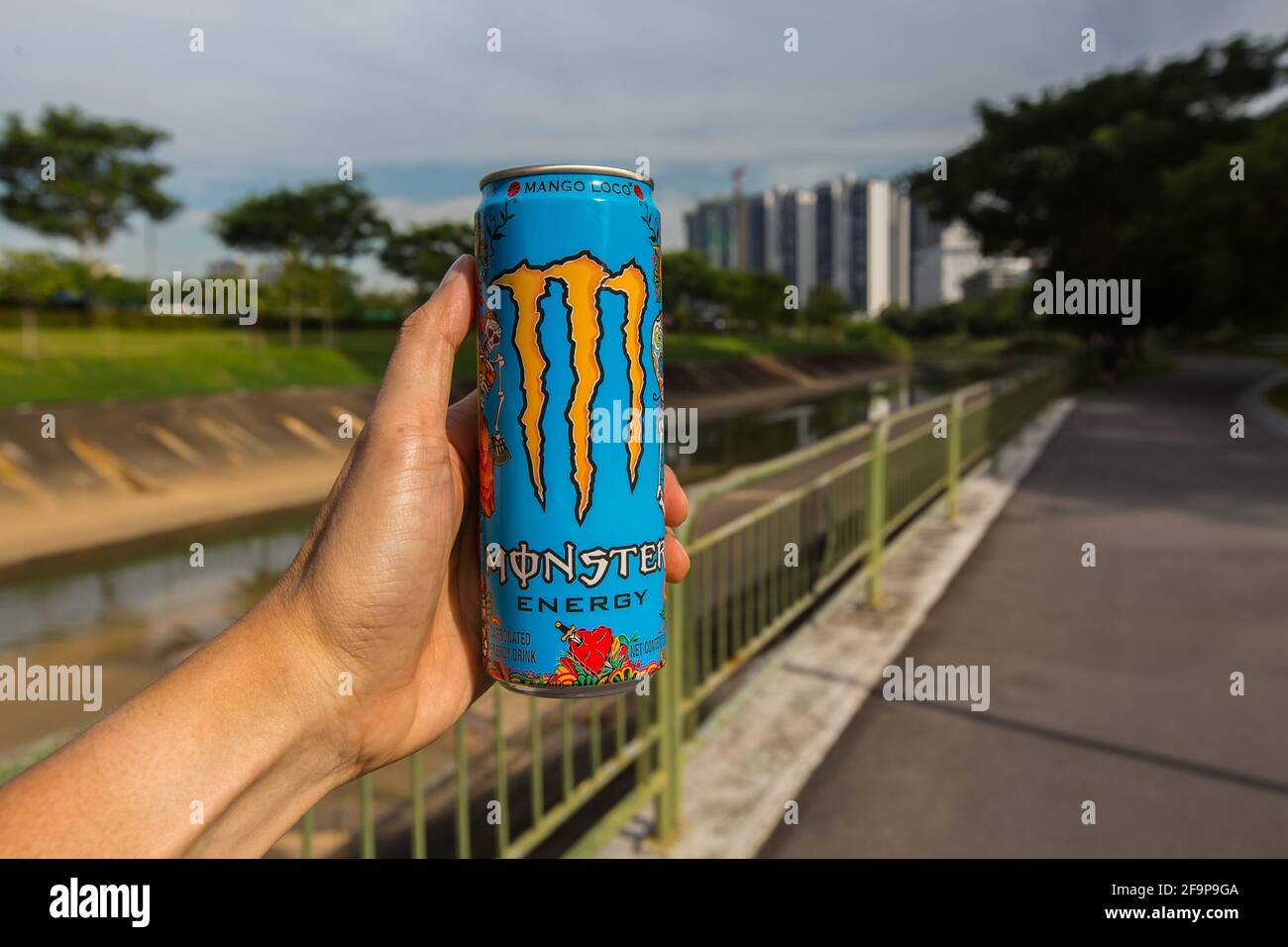Eine Hand, die eine Monster Energy hält, trinkt in einem Park. Singapur. Stockfoto