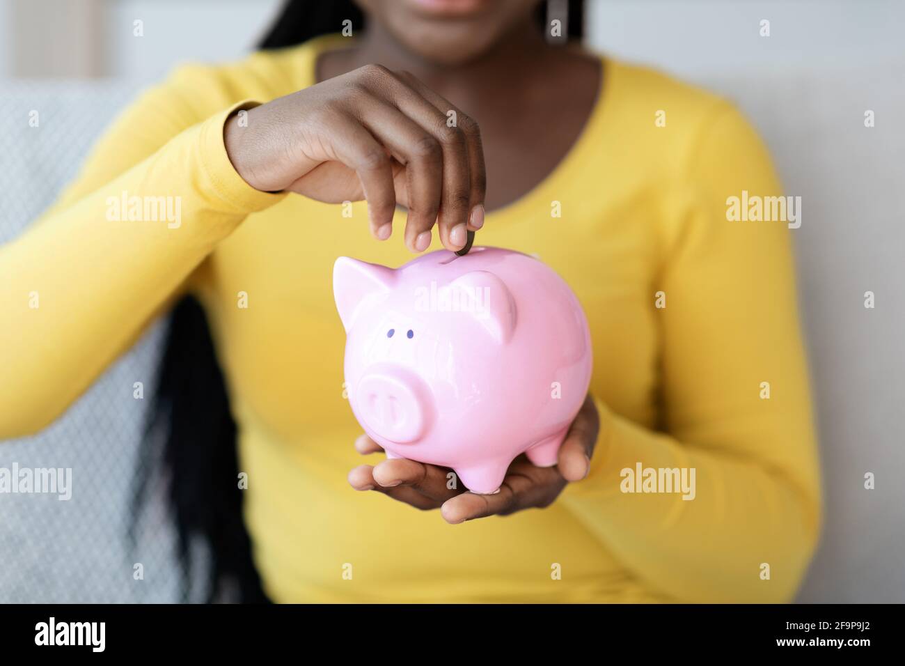 Geldeinsparungen. Nahaufnahme Von Black Woman Putting Coin To Piggy Bank Stockfoto