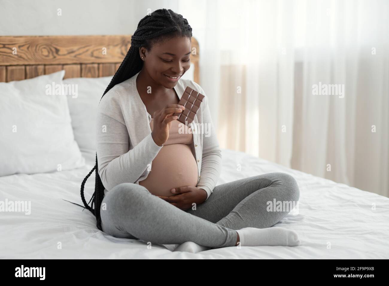 Süßer Zahn. Glückliche schwarze schwangere Frau genießen essen Schokolade im Bett Stockfoto