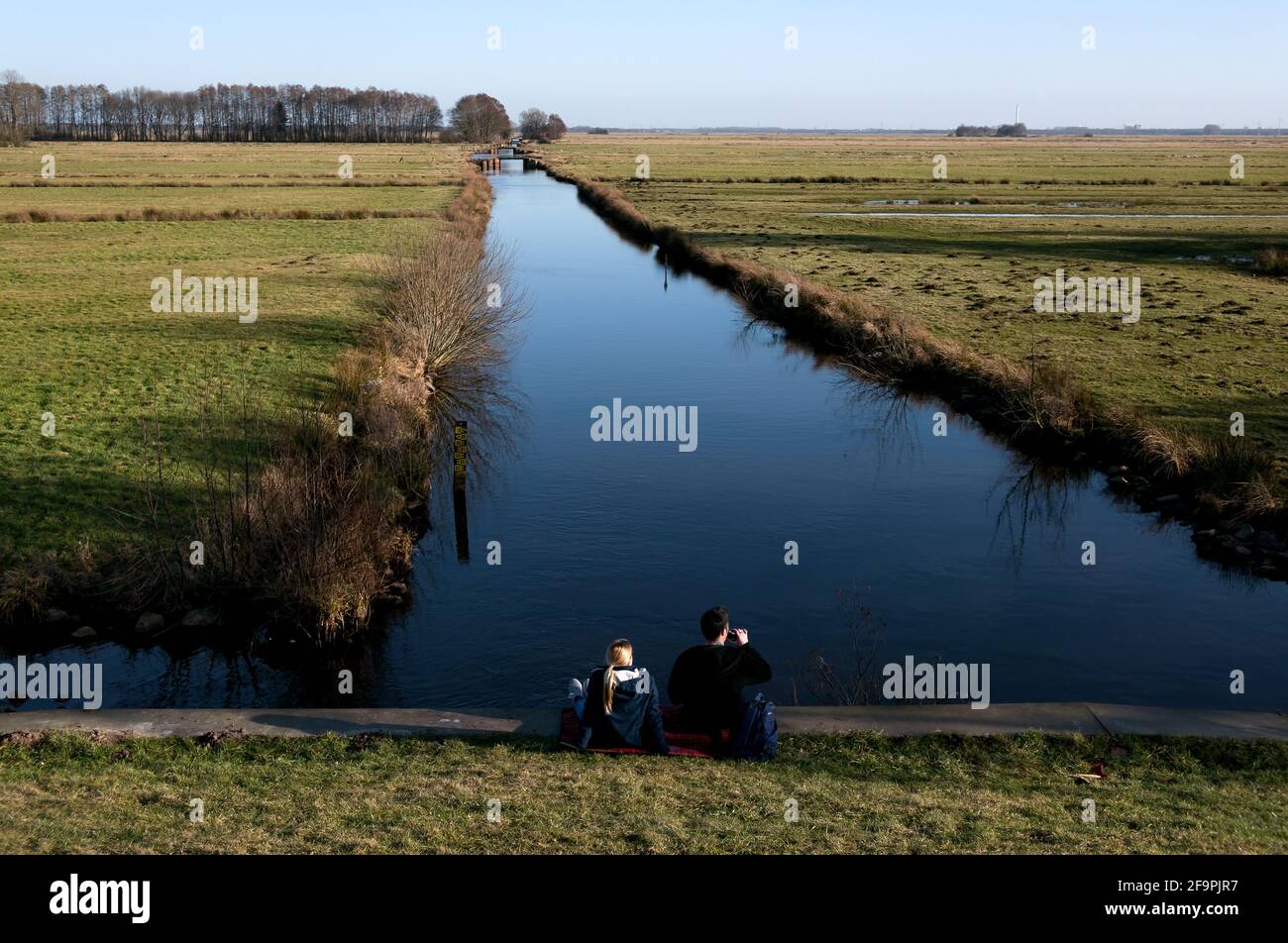 24.02.2021, Bremen, Bremen, Deutschland - Junge Menschen sitzen an einem Abflussgraben mit Blick auf das Hollerland. 00A210224D083CAROEX.JPG [ Stockfoto
