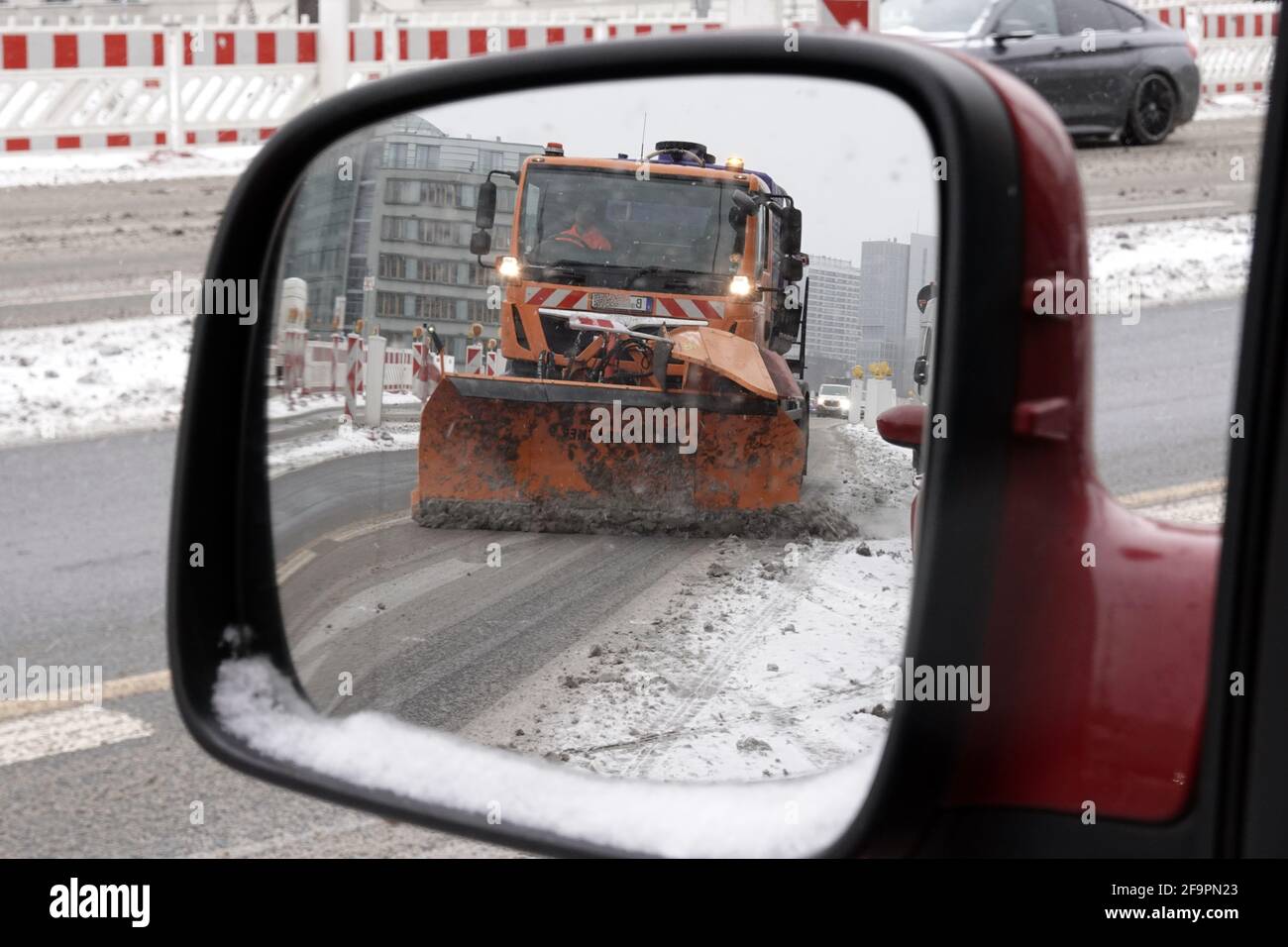 07.02.2021, Berlin, , Deutschland - der BSR-Winterdienst spiegelt sich im linken Seitenspiegel eines Autos beim Räumen einer Straße wider. 00S210207D492CAROEX.JPG [MOD Stockfoto