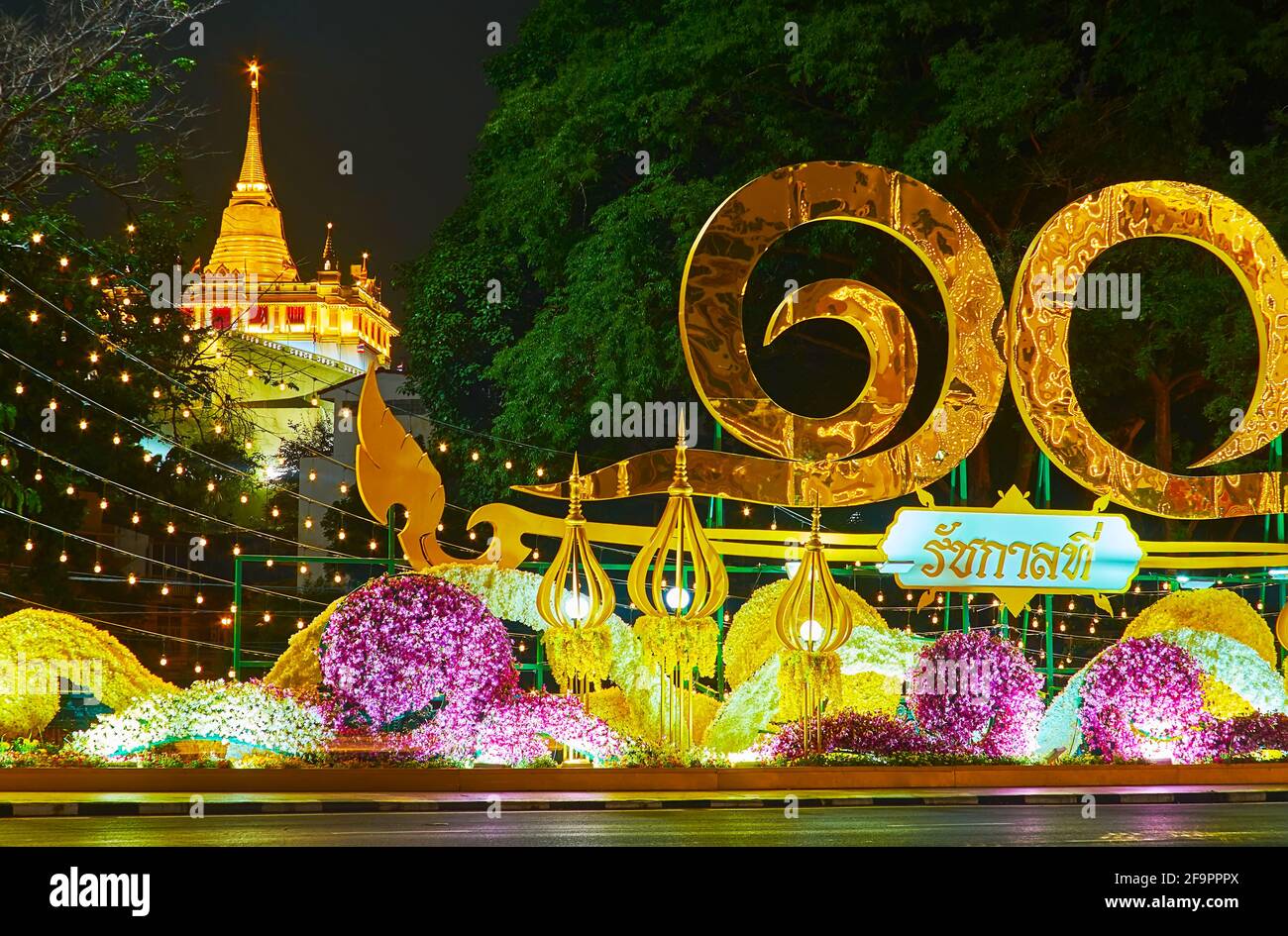 Die Phan Fa Lilat Brücke ist mit einer szenischen Installation dekoriert, die auf die Krönung von König Rama X zurückzuführen ist, die Golden Mount Temple Stupa ist hinter der zu sehen Stockfoto