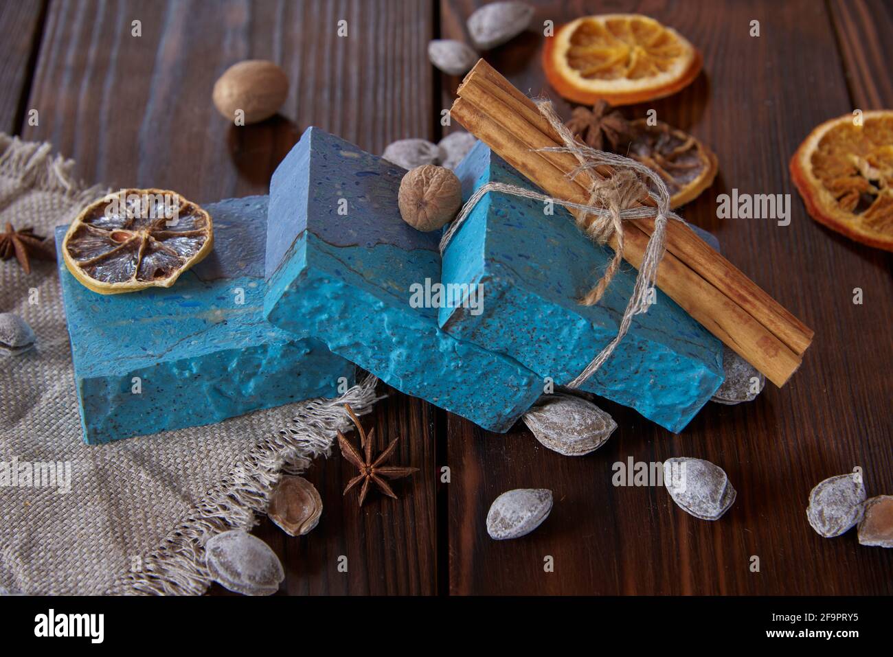 Helle, duftende blaue handgemachte Seife, verschiedene Gewürze und Nüsse auf der dunklen Holzplatte. Stockfoto