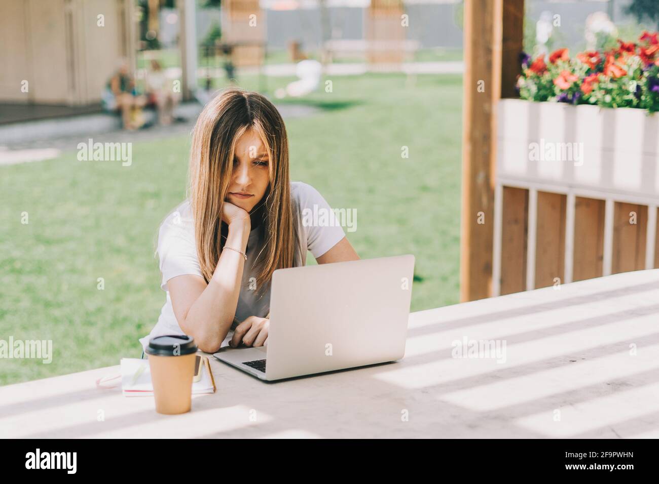 Schöne Frau arbeitet an Notebook sitzen auf der Bank draußen und trinken Kaffee. Mit Computer und Online-Shops. Glückliche Dame Mädchen mit hellen Haaren Stockfoto
