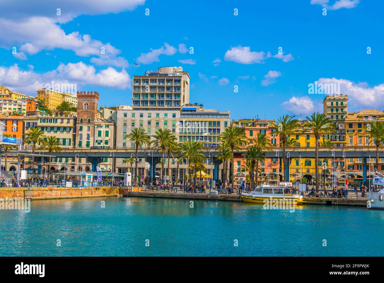 Die Menschen schlendern über die Strandpromenade, die durch den Hafen von genua führt. Der Hafen bietet verschiedene Attraktionen für Touristen wie die europäischen größten Stockfoto