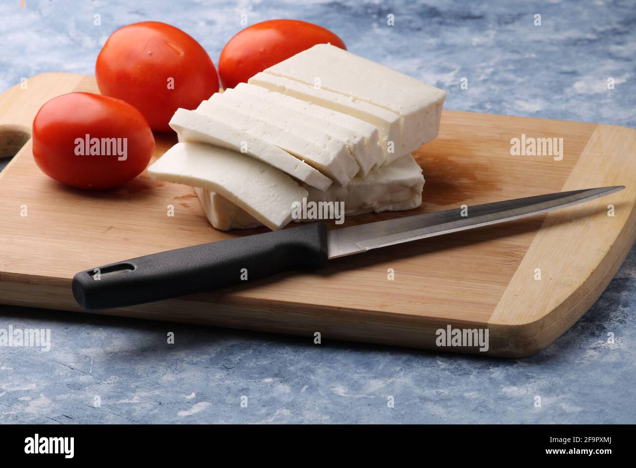 Frisch geschnittener Paneer oder Quark mit Tomaten und Messer auf Schneidebrett. Stockfoto