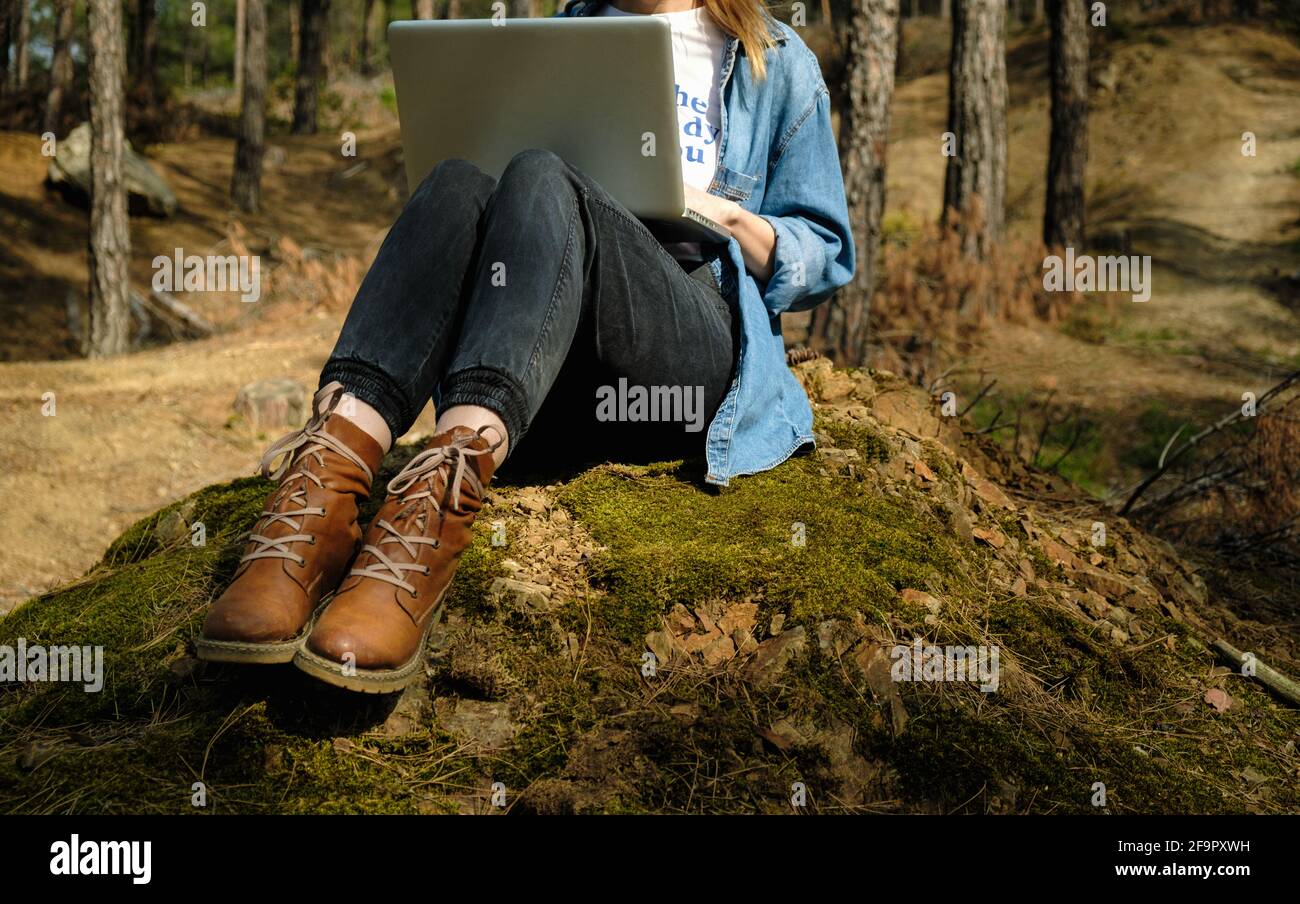 Junge Frau, die am Wald auf dem Boden sitzt und am Laptop arbeitet. Stockfoto