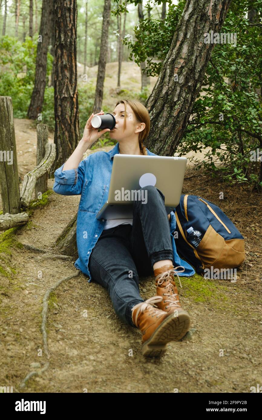 Junge Frau, die am Wald auf dem Boden sitzt und am Laptop arbeitet. Stockfoto
