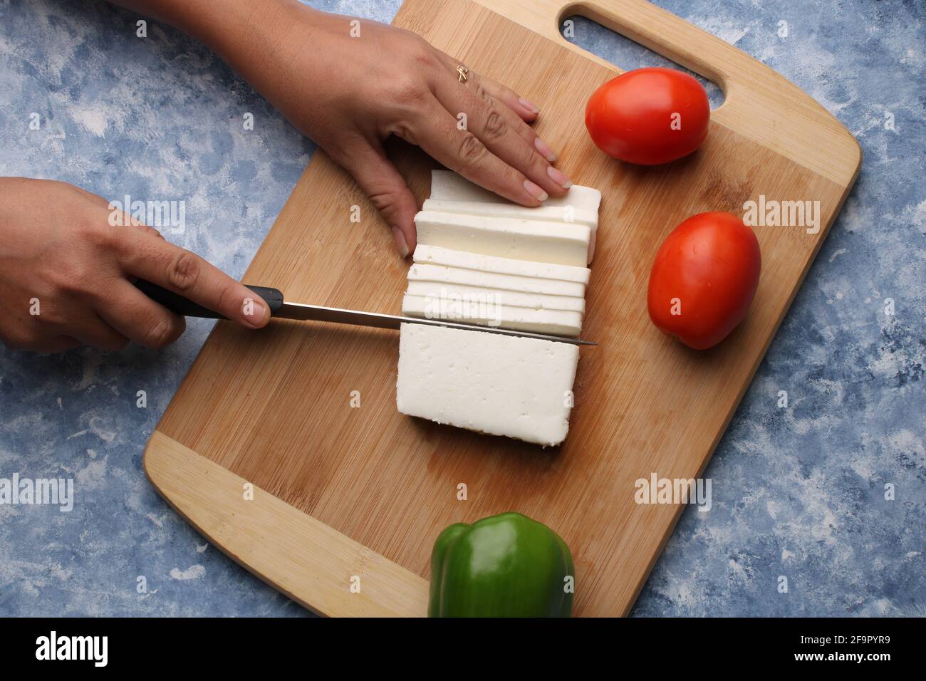 Paneer oder Quark mit Tomaten, Paprika und einem Messer auf einem hölzernen Schneidebrch. Stockfoto