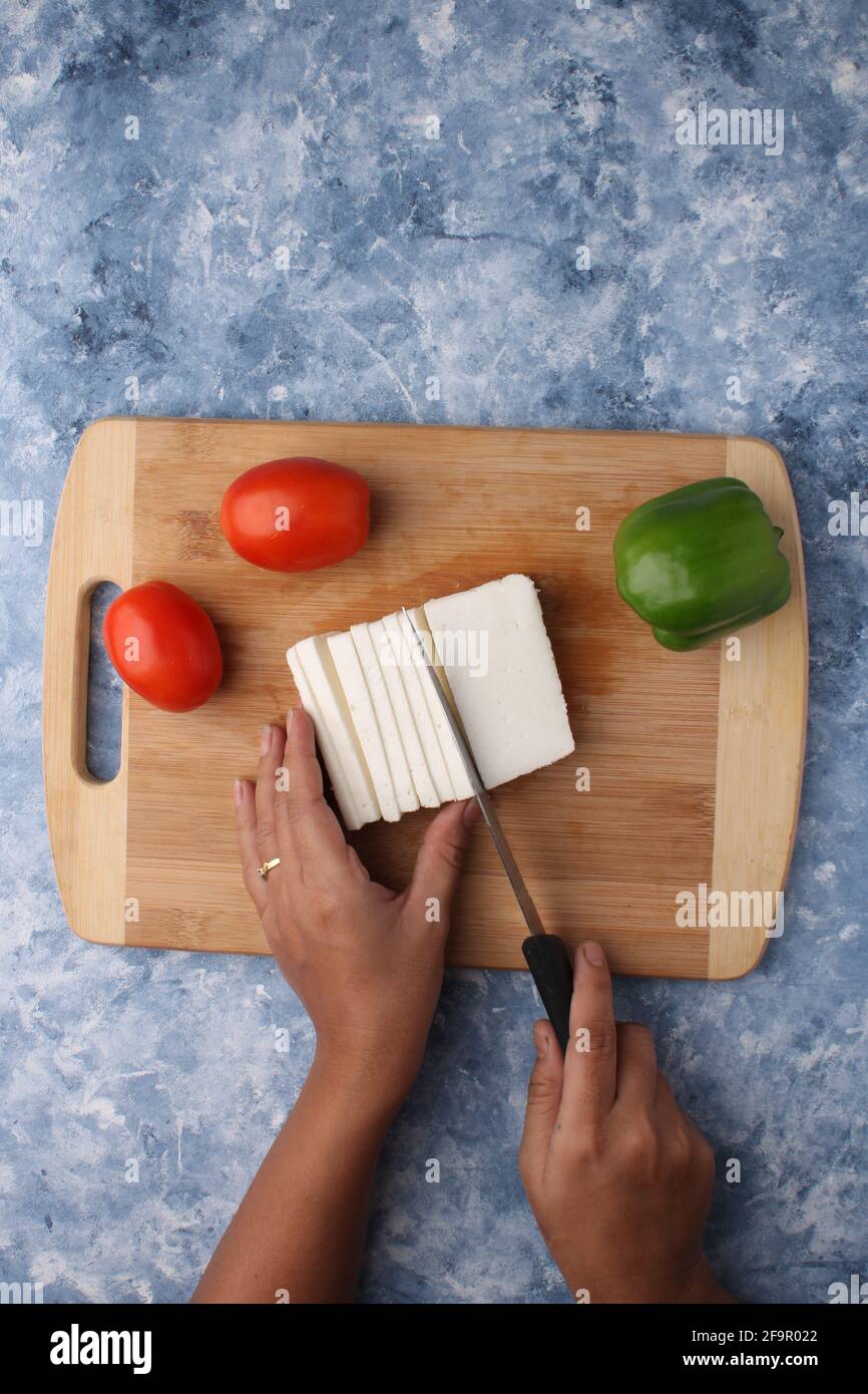 Paneer oder Quark mit Tomaten, Paprika und einem Messer auf einem hölzernen Schneidebrch. Stockfoto