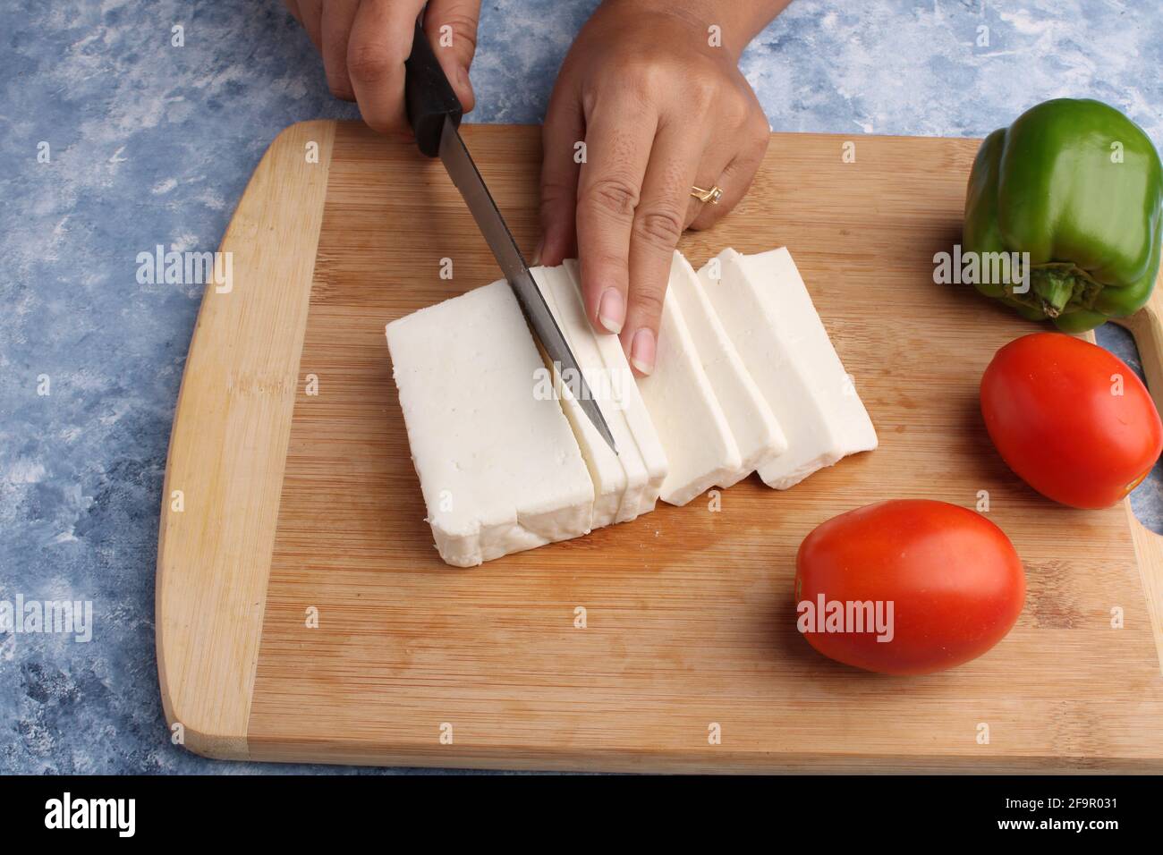 Paneer oder Quark mit Tomaten, Paprika und einem Messer auf einem hölzernen Schneidebrch. Stockfoto