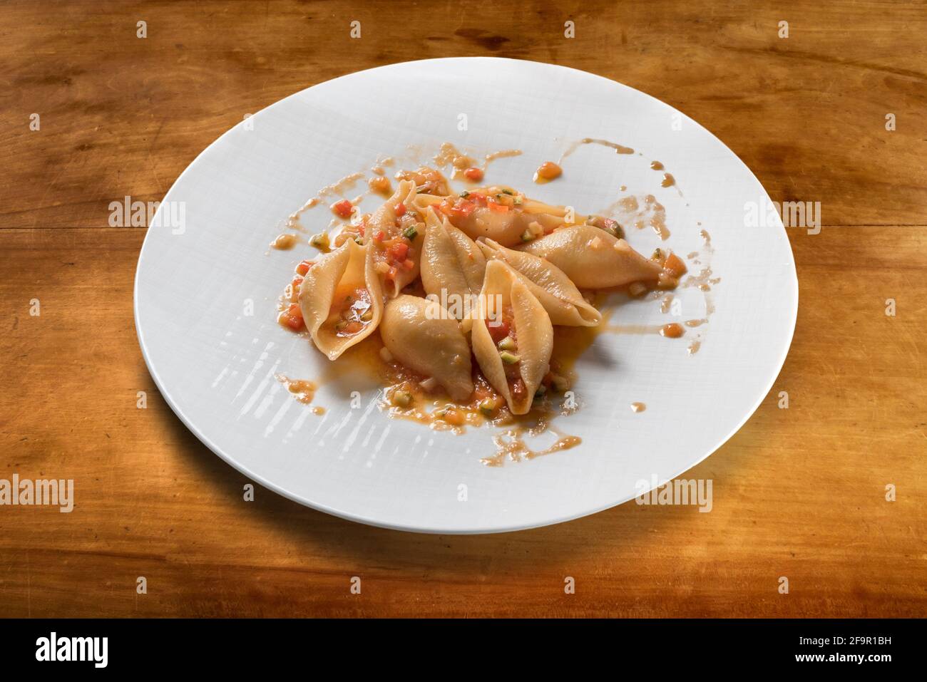 Italienische Pasta Conchiglioni gekocht mit Tomatensauce und Gemüse in Weißer Teller auf Holztisch Stockfoto