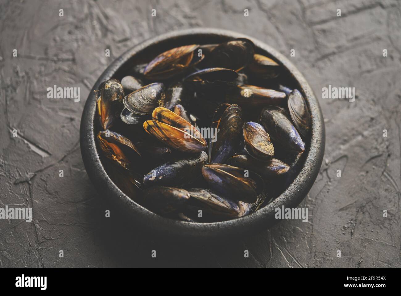 Frische und rohe Meeresmuscheln in schwarzer Keramikschale platziert Auf dunklem Steingrund Stockfoto