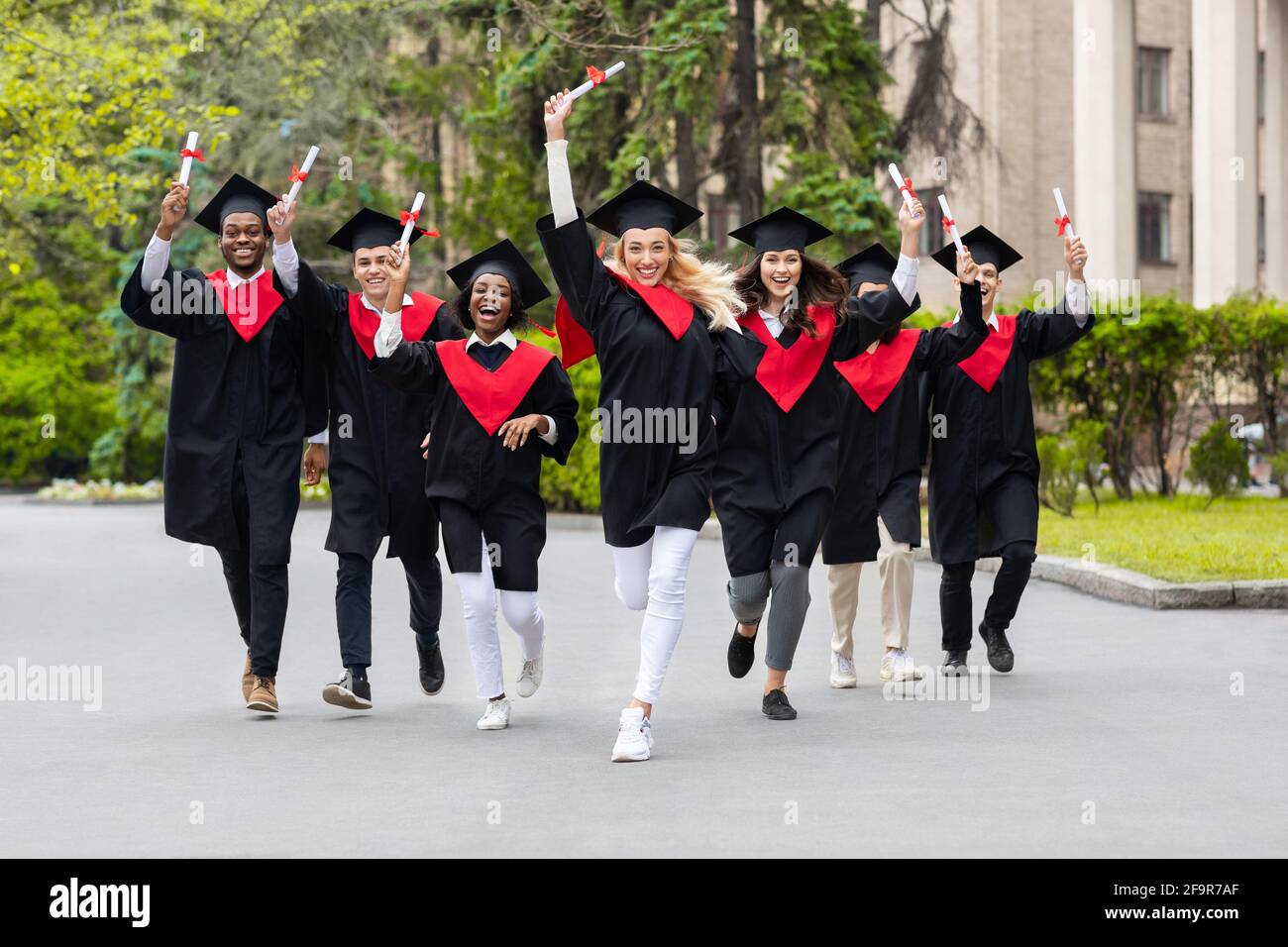 Glückliche multirassische Gruppe von Studenten, die Diplome sammeln und laufen Stockfoto