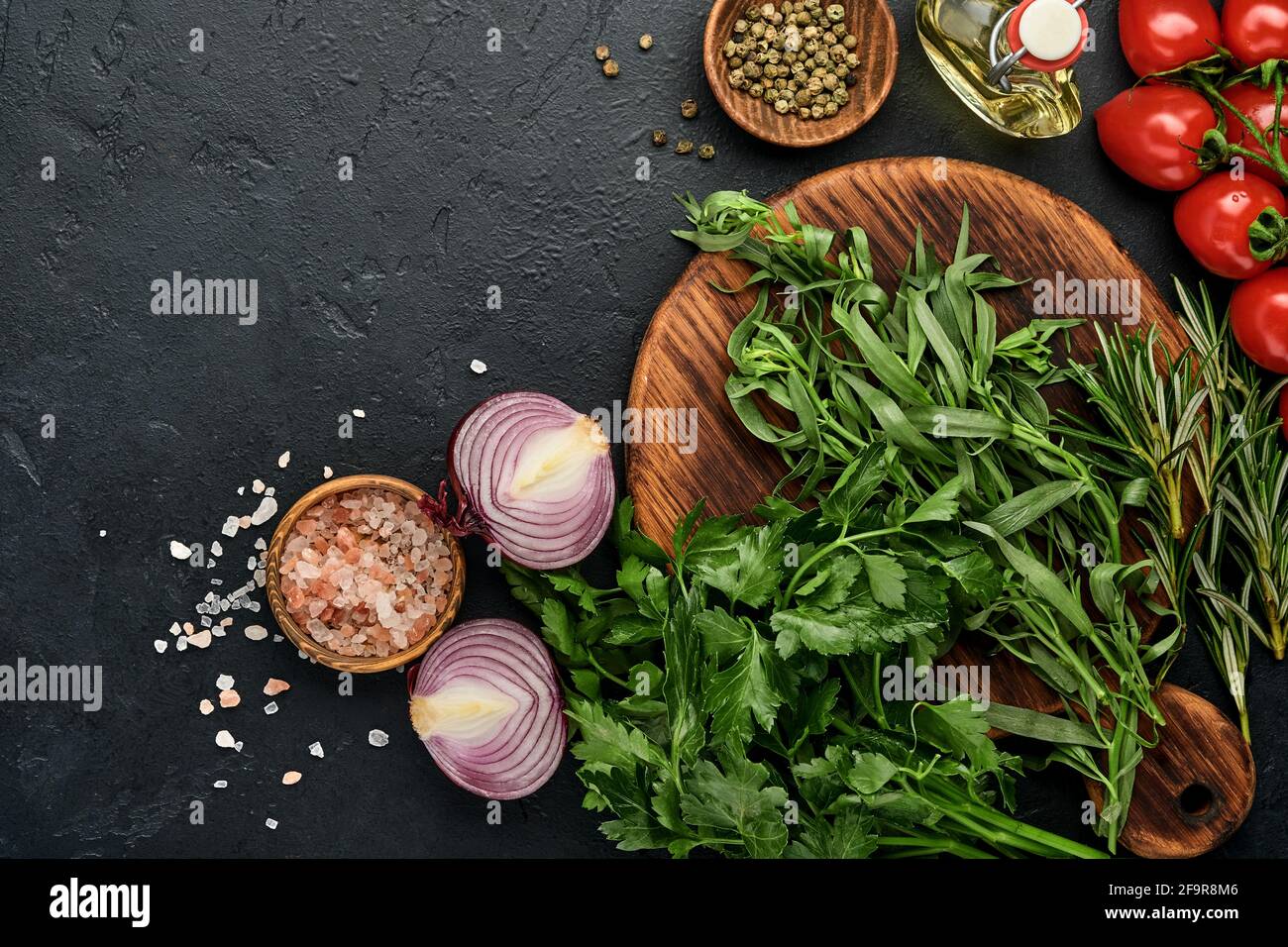 Frischer Estragon. Zweig der frischen Kräuter Gewürz-und Kochprodukte, Tomaten, Paprika, Zwiebeln und Olivenöl auf schwarzem Beton Hintergrund. Kochen Bac Stockfoto