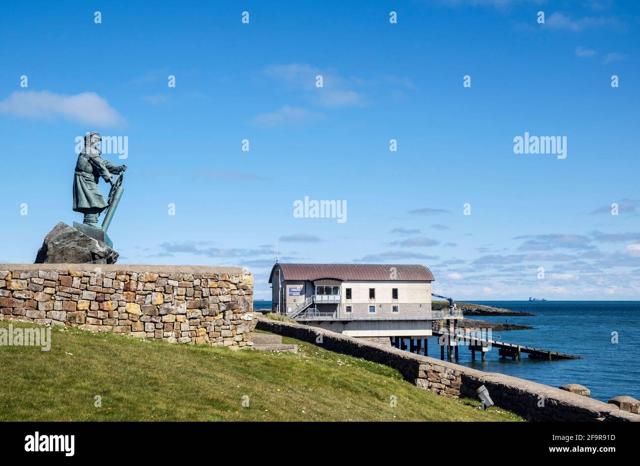 Statue von Coxswain Richard (DIC) Evans 1905-2001 mit neuer Lifeboat Station im Hintergrund. Moelfre, Isle of Anglesey, Wales, Großbritannien Stockfoto