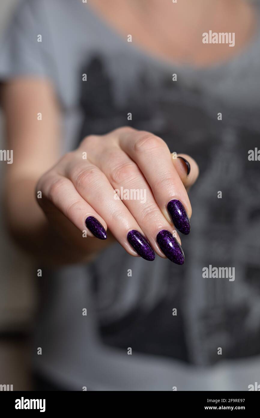 Weibliche Hand mit langen Nägeln und dunkelvioletter Flieder-Maniküre Fasst  eine Flasche Nagellack Stockfotografie - Alamy