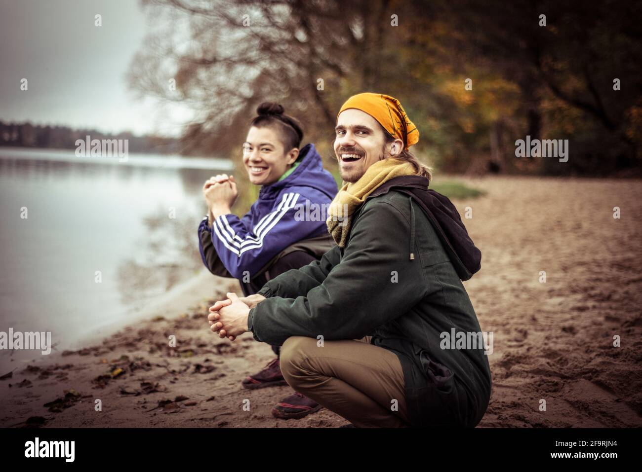 Zwei fröhliche, schwule Freunde sitzen im Winter lachend am See Und chatten Stockfoto