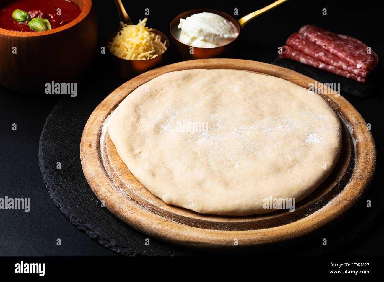 Food-Konzept hausgemachter Pizzateig und Pizzazutaten auf Holz Platine auf schwarzem Hintergrund mit Kopierplatz Stockfoto