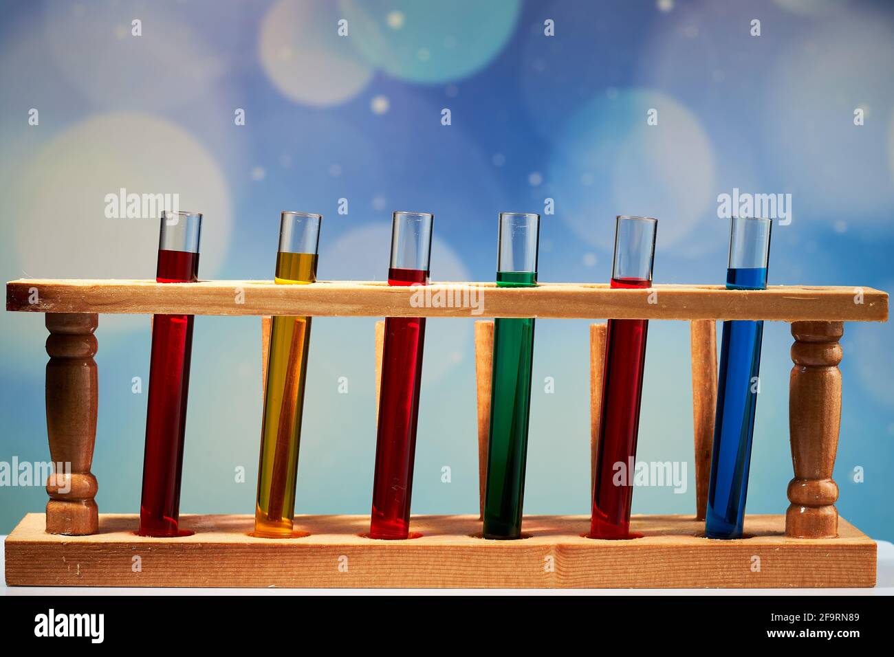 Rote, gelbe, grüne und blaue Getränke in den Reagenzgläsern auf einem Ständer. Blauer Hintergrund dahinter. Stockfoto