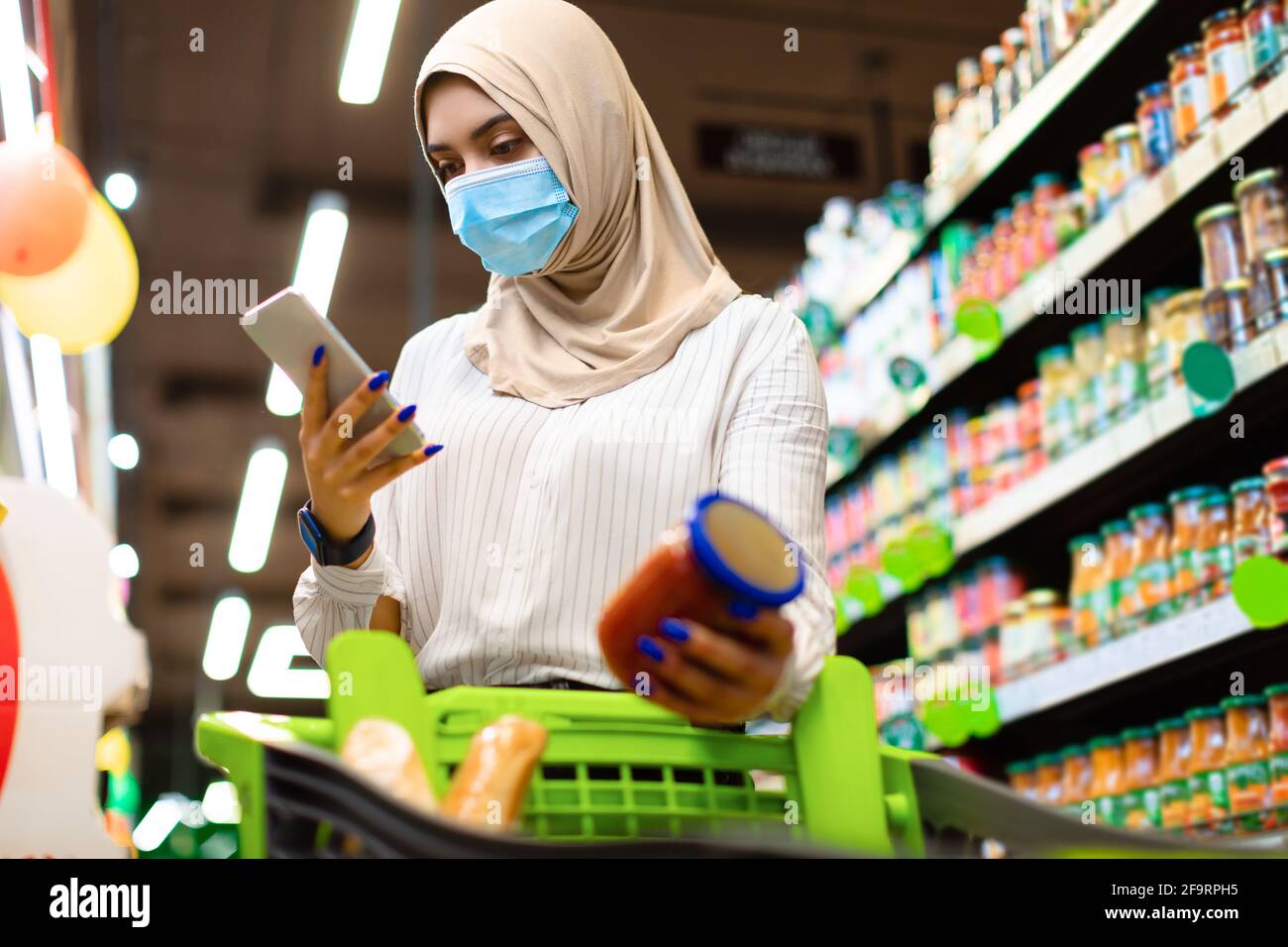 Muslimische Frau, Die Smartphone Beim Einkaufen Im Lebensmittelgeschäft Verwendet Stockfoto