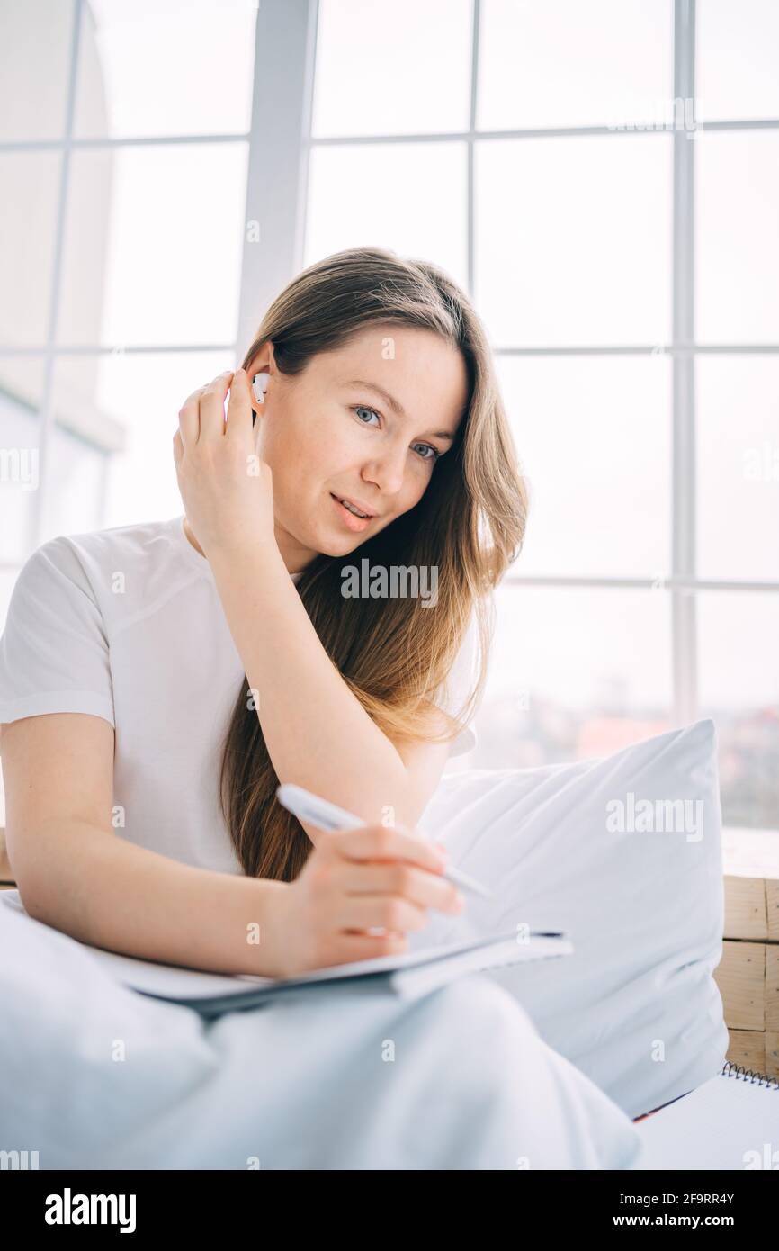 Mädchen schreibt in einem Notizbuch und hört Musik in Bett Stockfoto