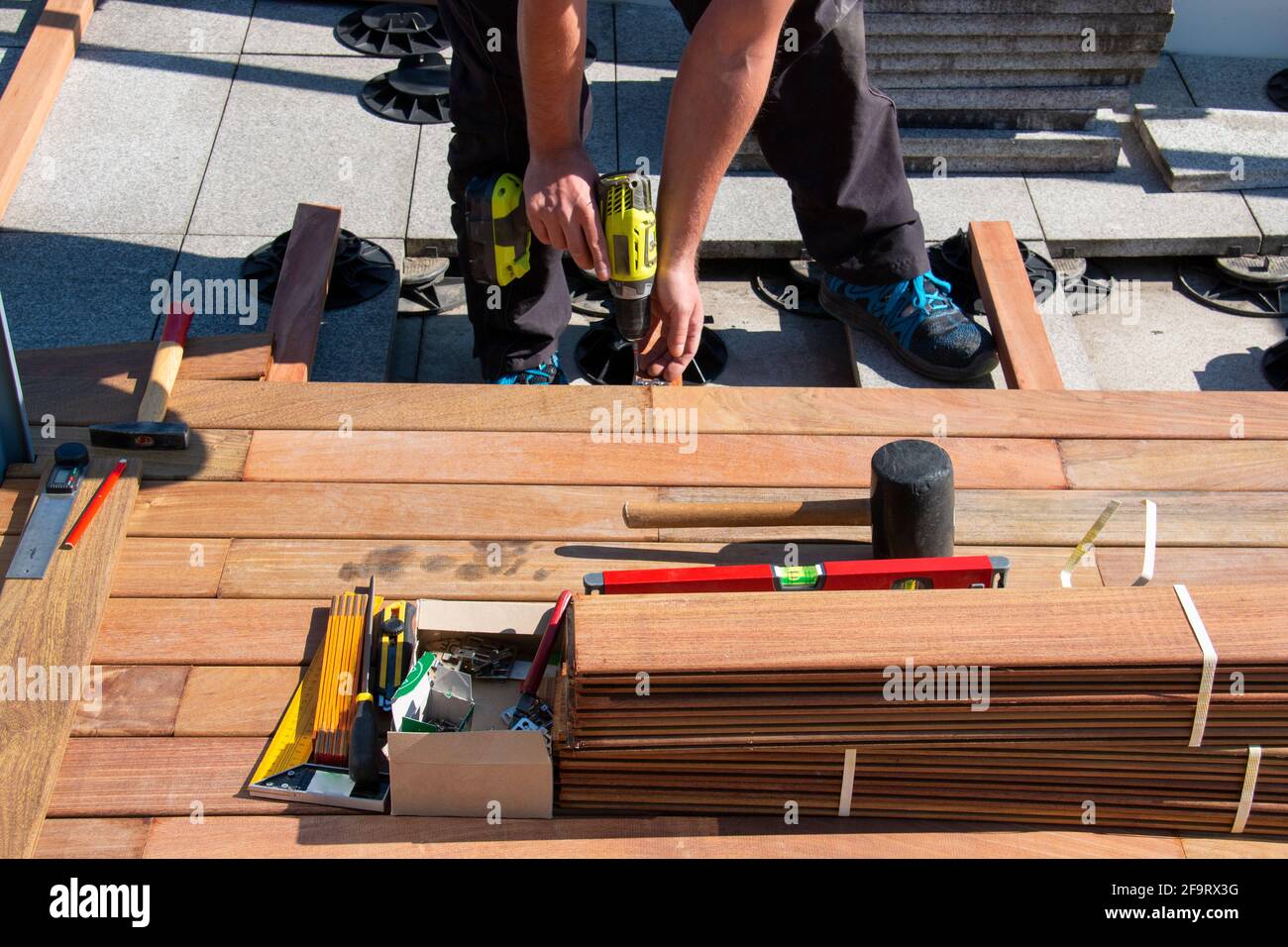 IPE Holz Terrasse Deck Konstruktion, Blick auf Tischlerhände mit einem Schraubendreher und Holzbearbeitungswerkzeuge während der Installation eines Deck, tropisches Hartholz Stockfoto