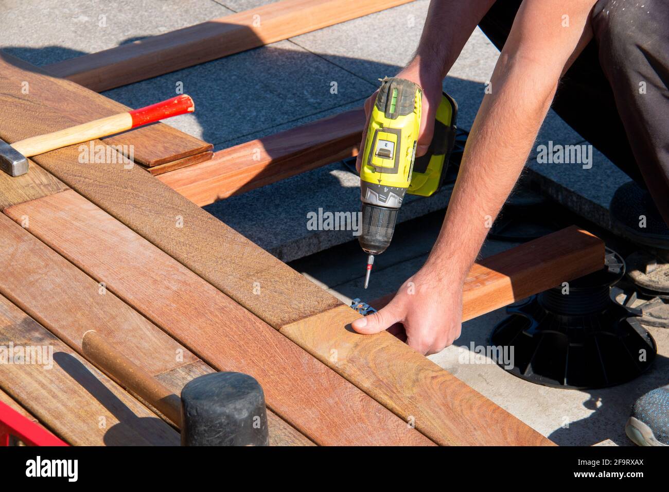IPE Holz Terrasse Deck Konstruktion, Handwerk Facharbeiter mit einem Power-Schraubendreher und Tischlerwerkzeuge Installation eines Decks, Hartholz-Deck Stockfoto