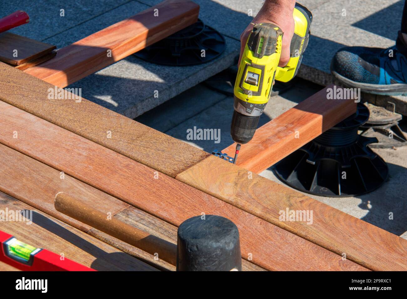 Hartholz Terrasse Deck Konstruktion - Baumeister Hand mit elektrischem Schraubendreher Nahaufnahme bei der Installation von exotischem ipe-Holzdeckenholz Platinen Stockfoto