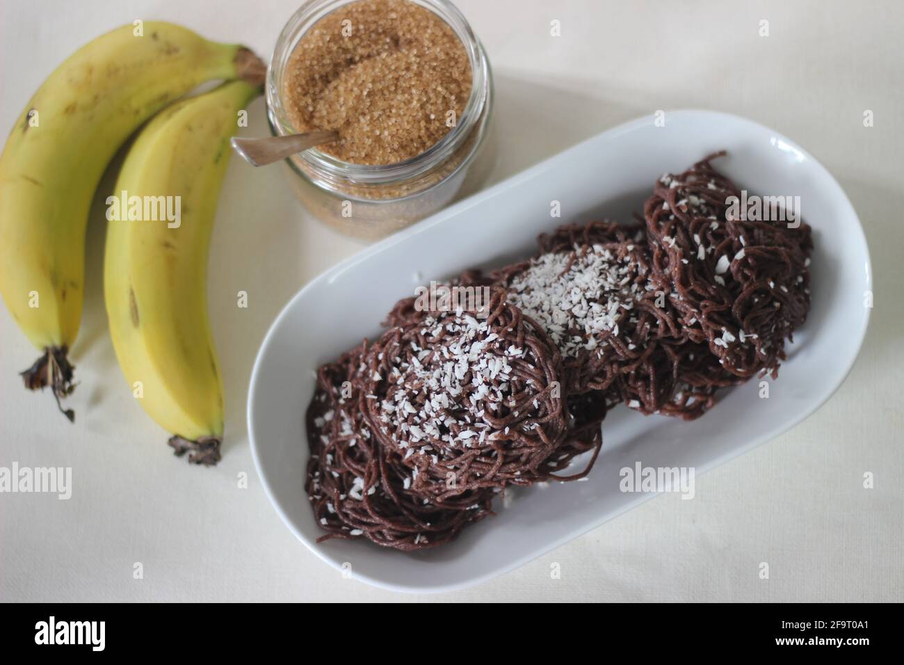 Schnur-Trichter aus Fingerhirse-Mehl. Gekrönt mit geriebener Kokosnuss. Serviert mit Banane und Zucker. Eine experimentelle Version eines Reisgericht von Ke Stockfoto