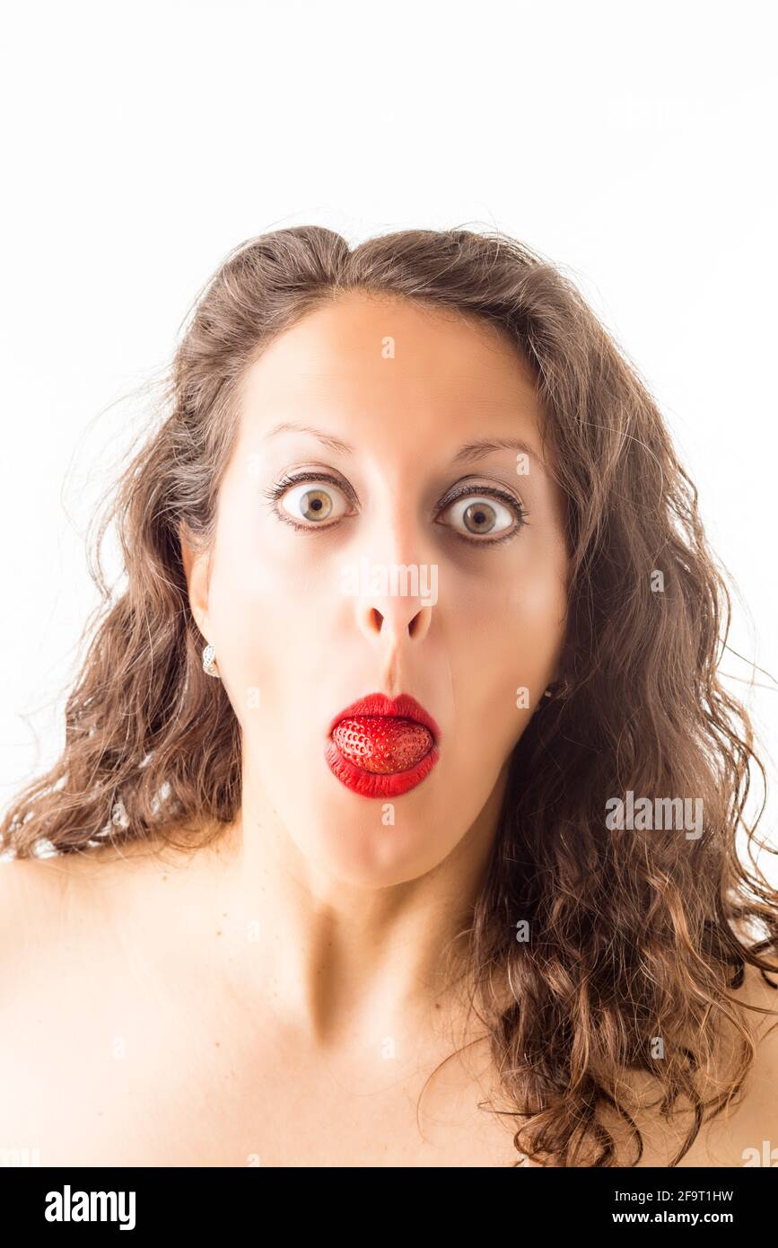 Porträt einer Frau mit einer Erdbeere im Mund als Zunge und einem überraschten Gesicht. Stockfoto